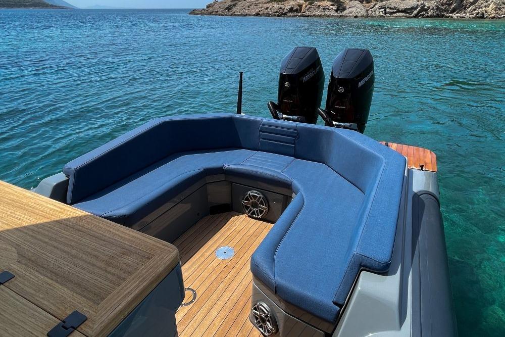 2026 Rock Marine RM 36 boat with blue seating, dual engines, and wooden deck on clear water.