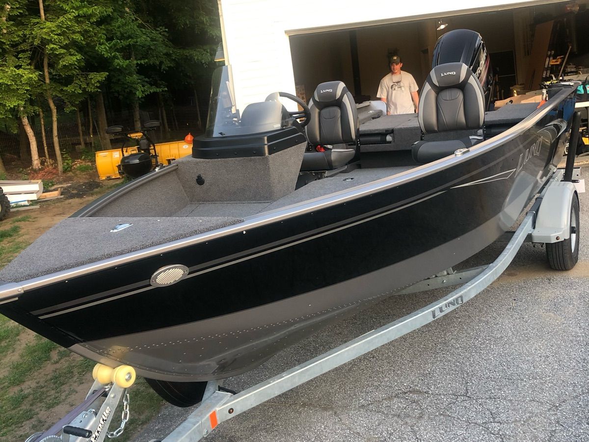 A black boat on a trailer, featuring two seats and an outboard motor.