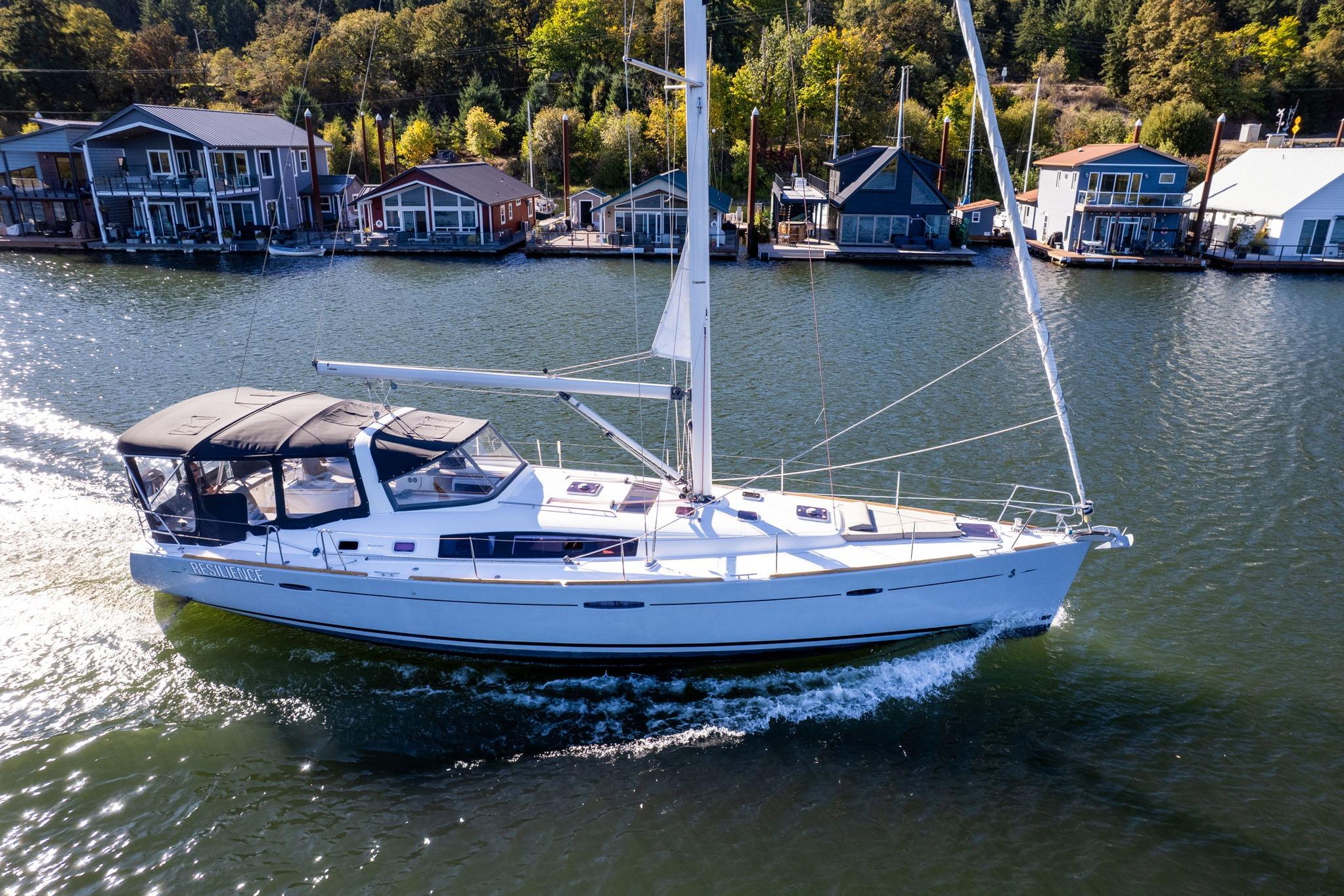 2013 Beneteau Oceanis 50 sailing near waterfront homes on a sunny day.