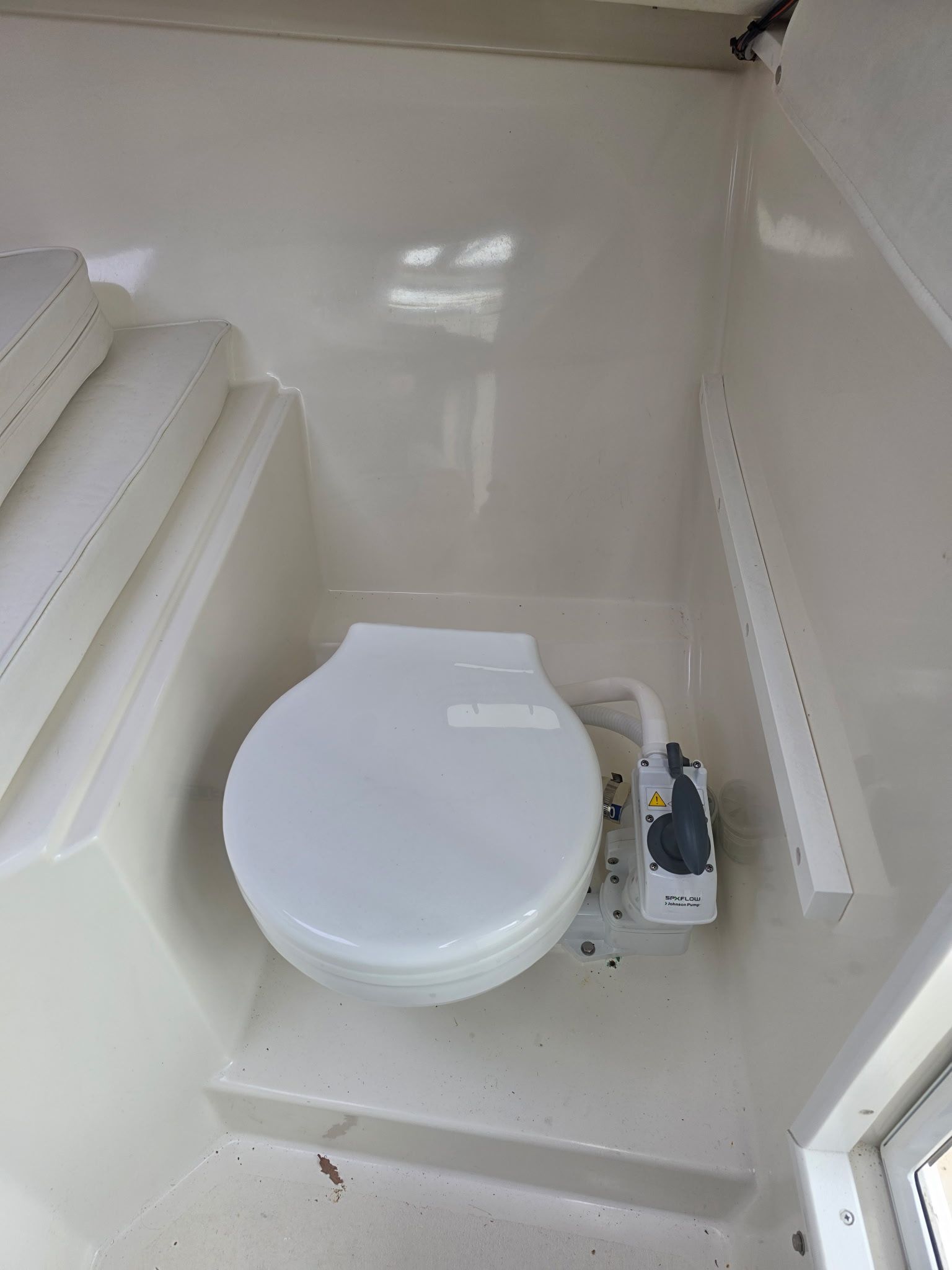 A white boat toilet in a small, clean space with cushioned seating.