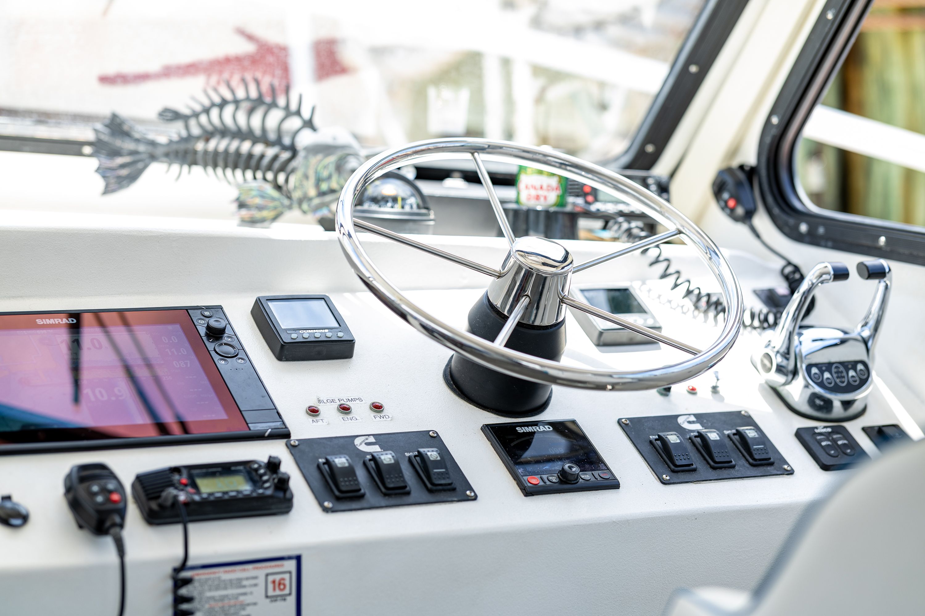 The image shows a boat's helm with a large steering wheel and various instruments.