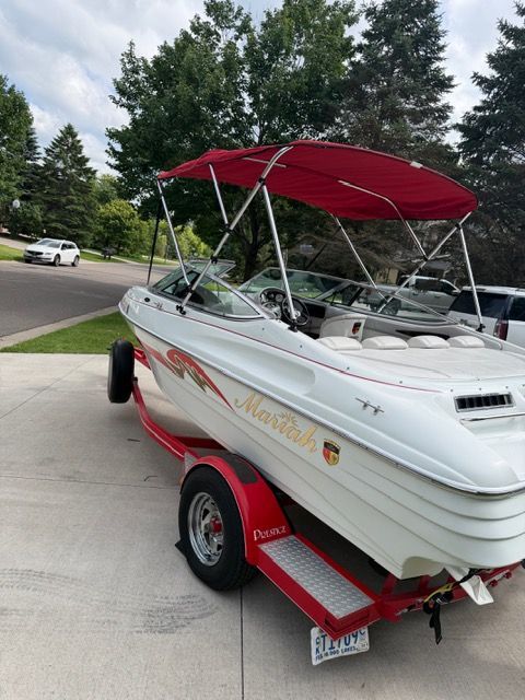 A white boat with a red canopy sits on a trailer in a driveway.