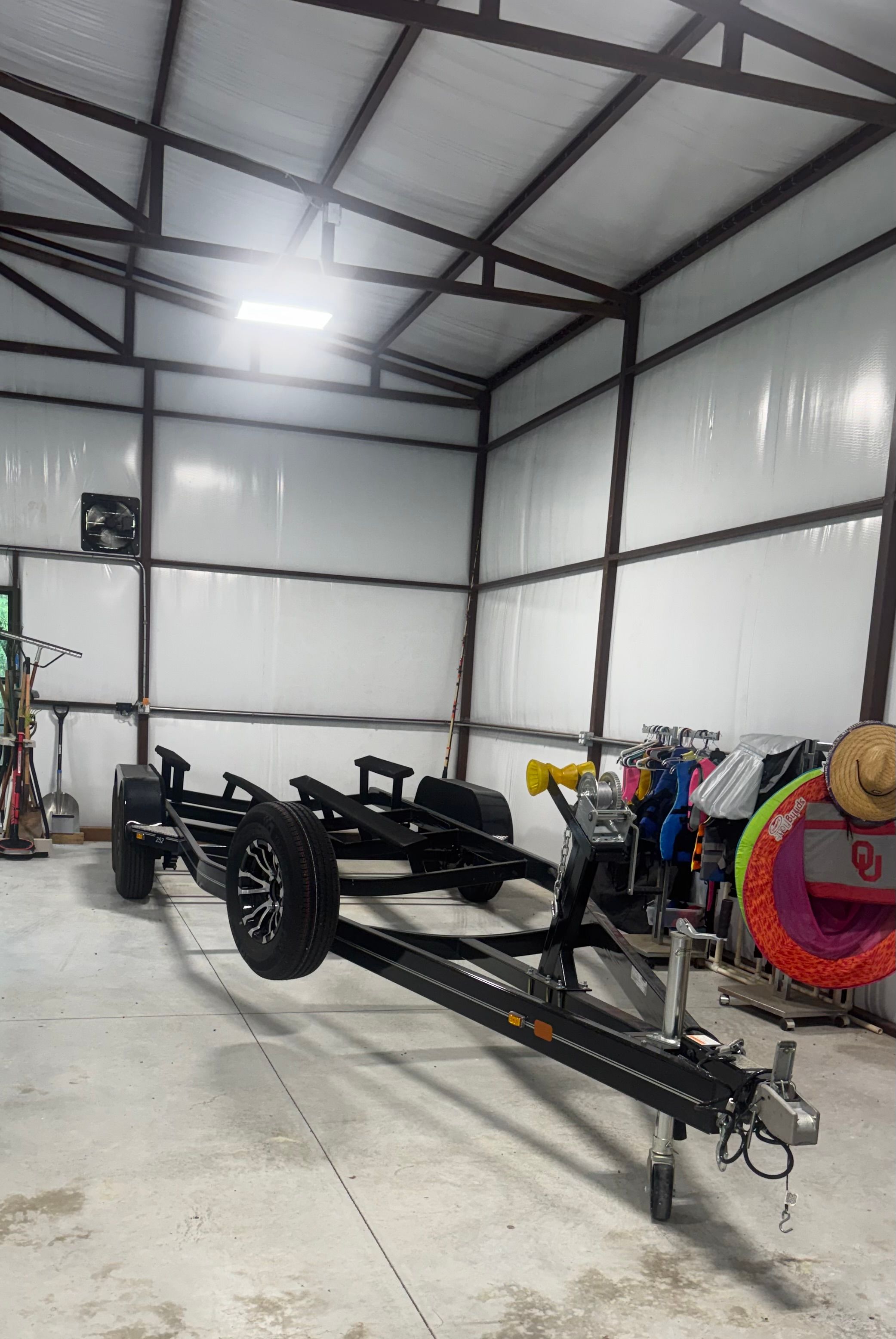 Boat trailer in a spacious garage with clothing and hats on the side.