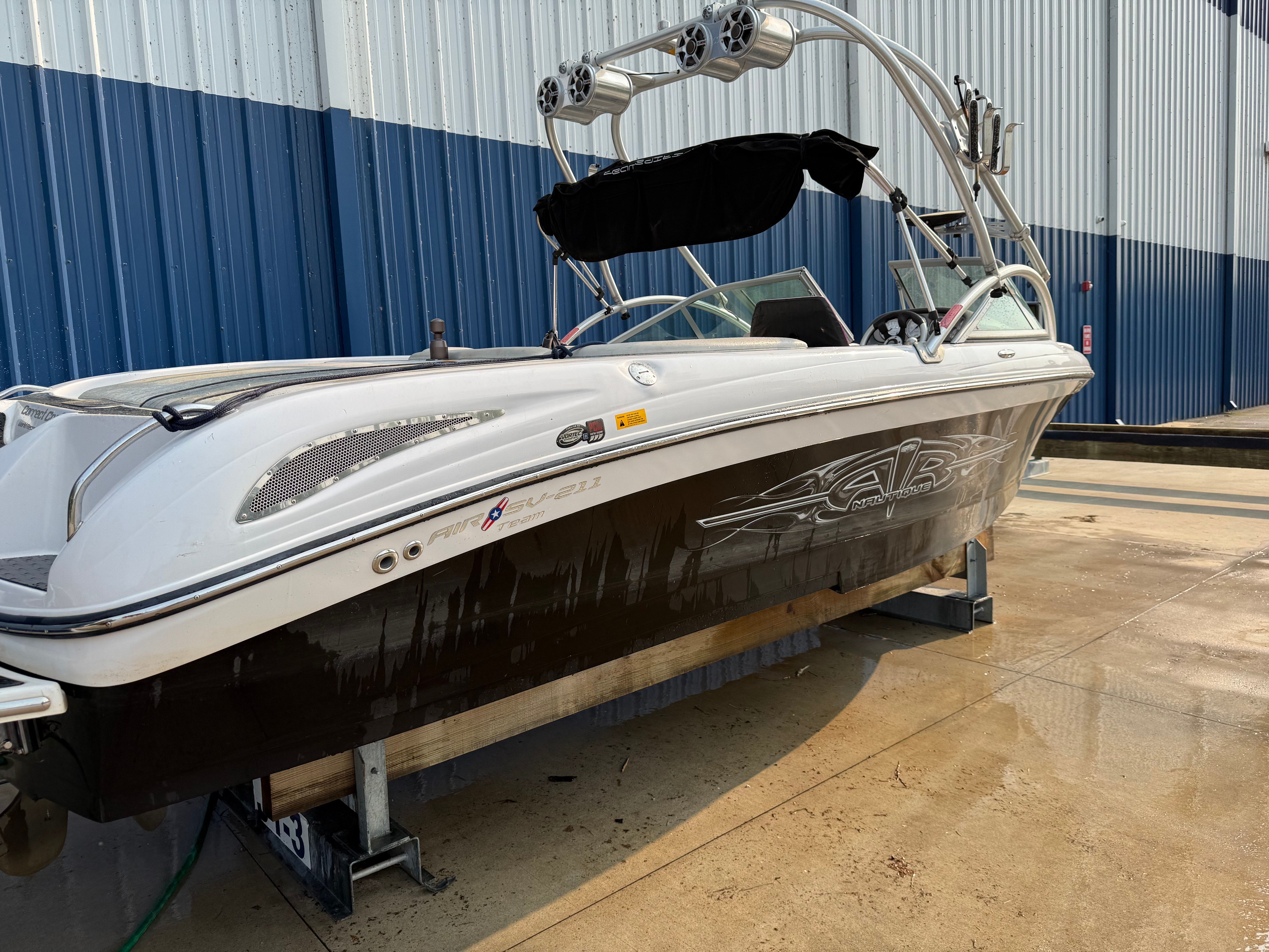 A white and black boat is on a dry dock in front of a blue building.