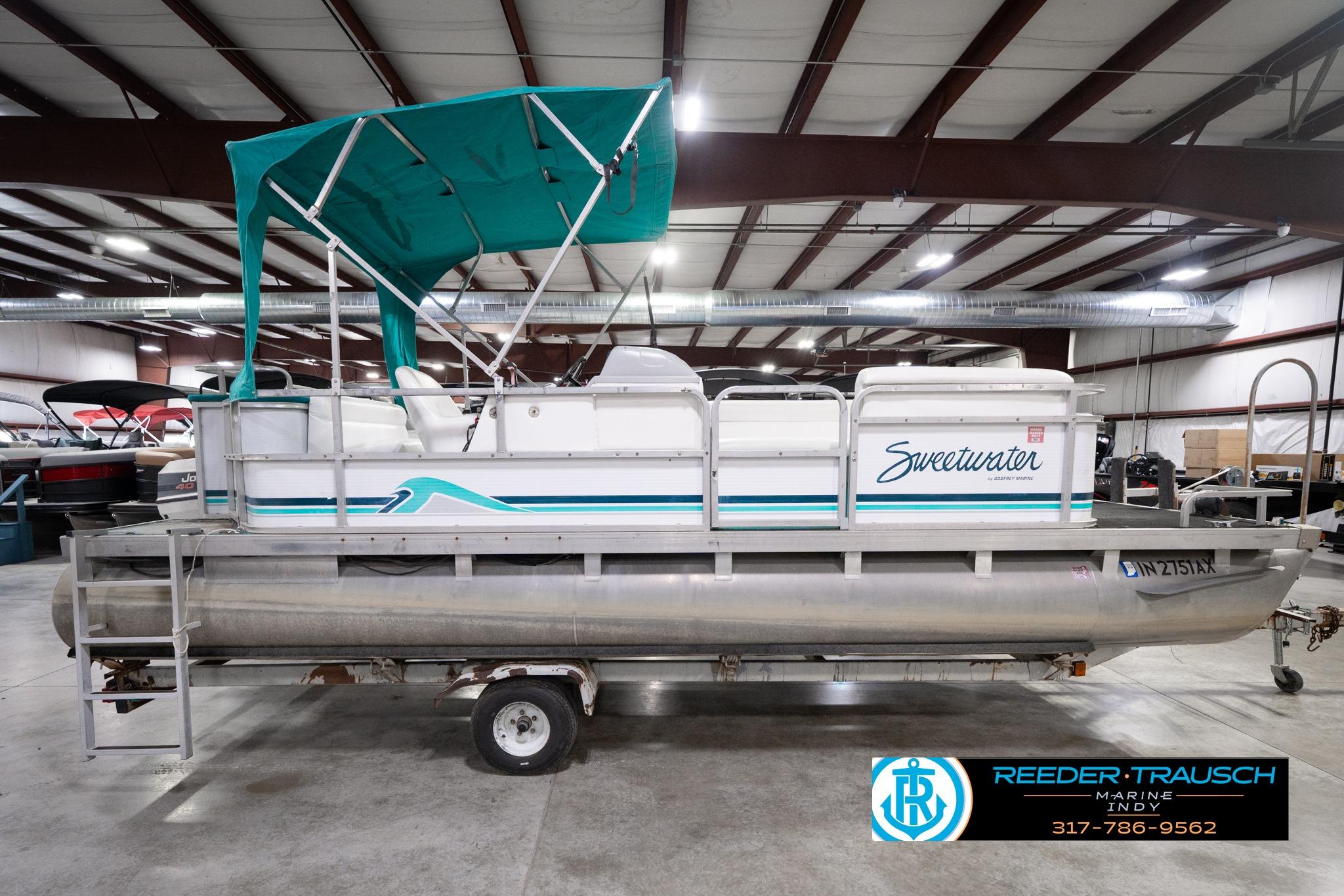 1992 Godfrey Sweetwater pontoon boat with teal canopy in indoor showroom.