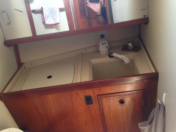 A sink with wooden cabinetry and mirror in a boat bathroom.