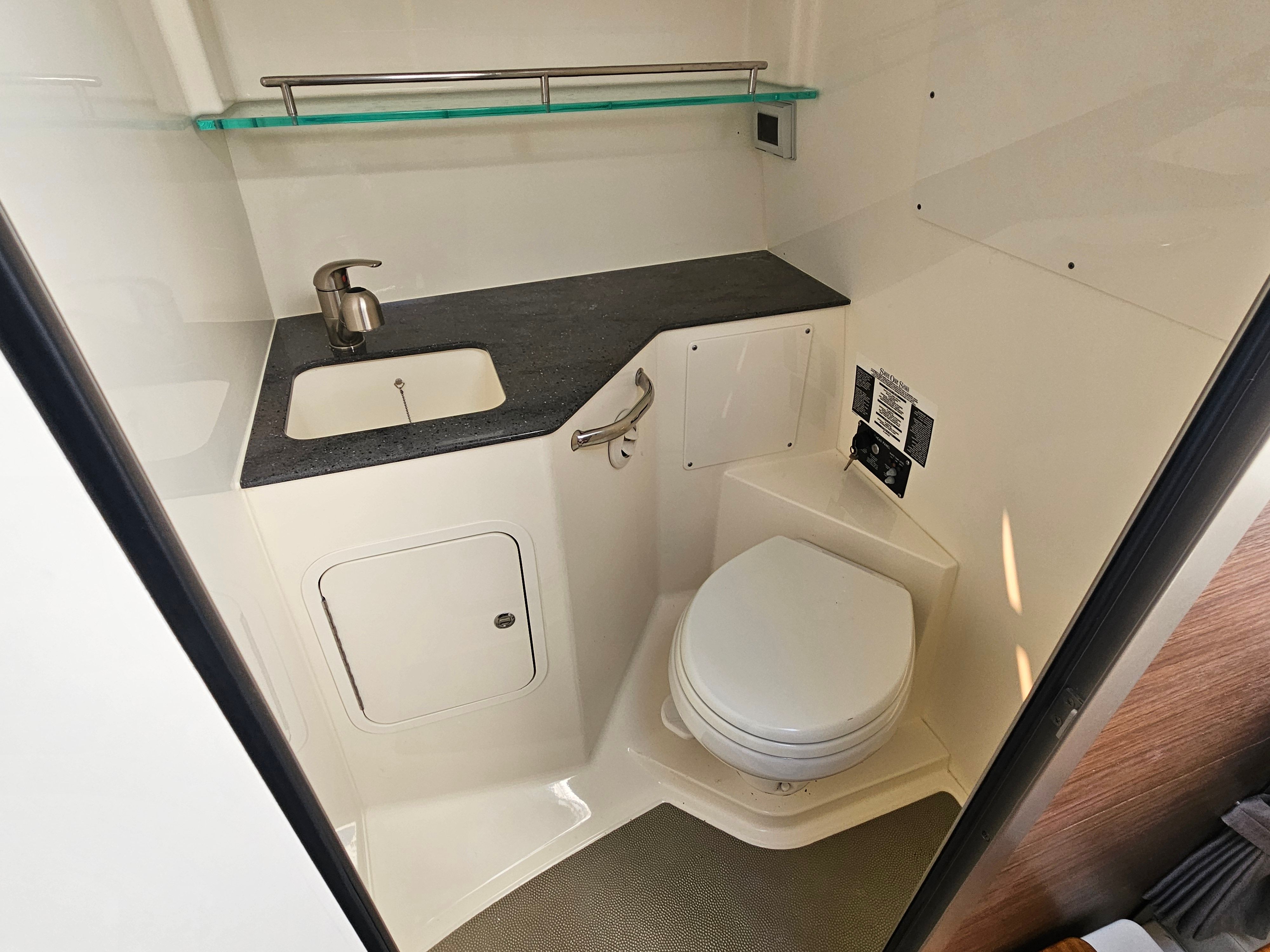 Interior view of a boat bathroom with sink, toilet, and counter space.