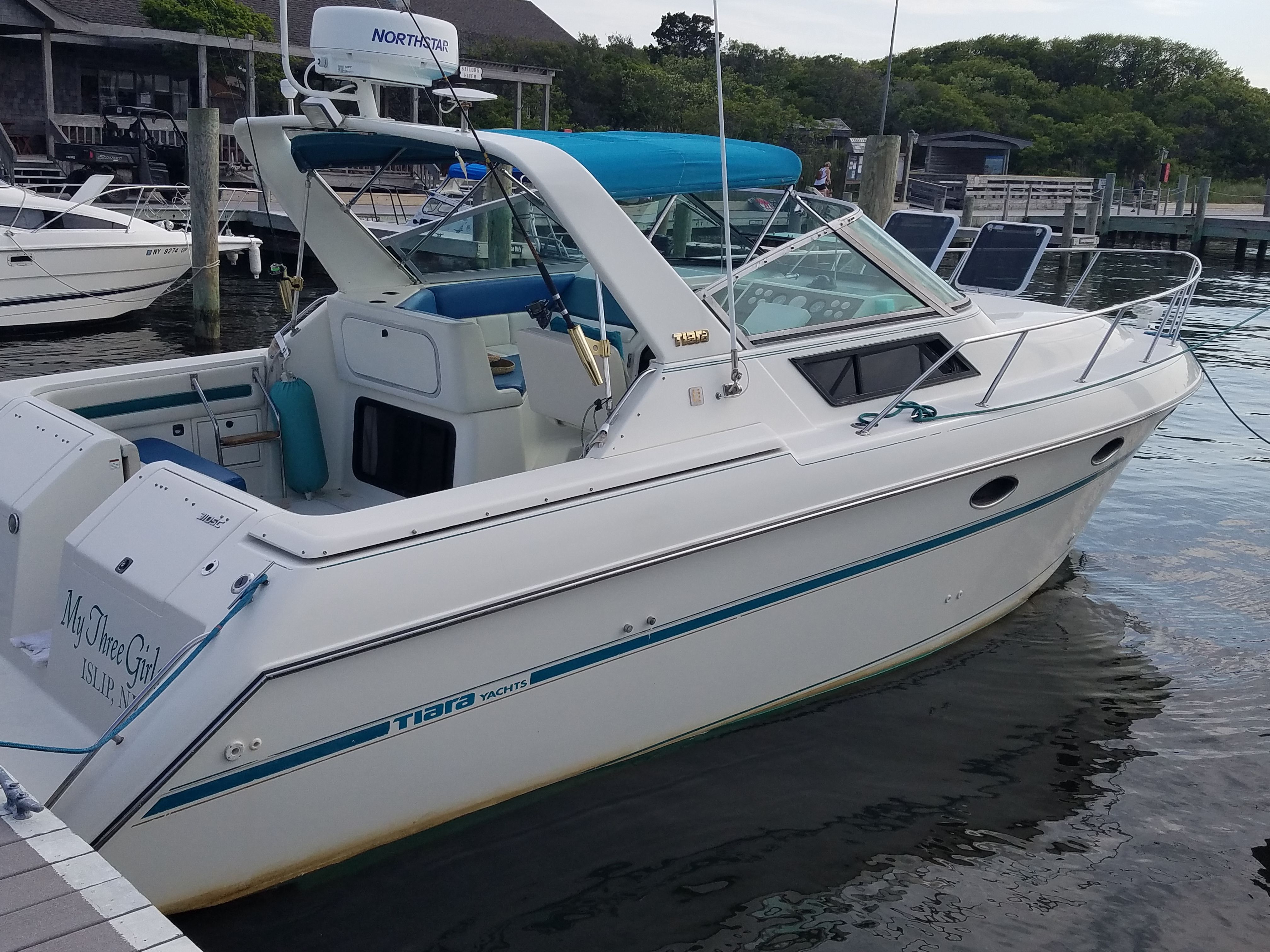 A 1989 Tiara Yachts Slickcraft docked, featuring a blue canopy and open cabin.