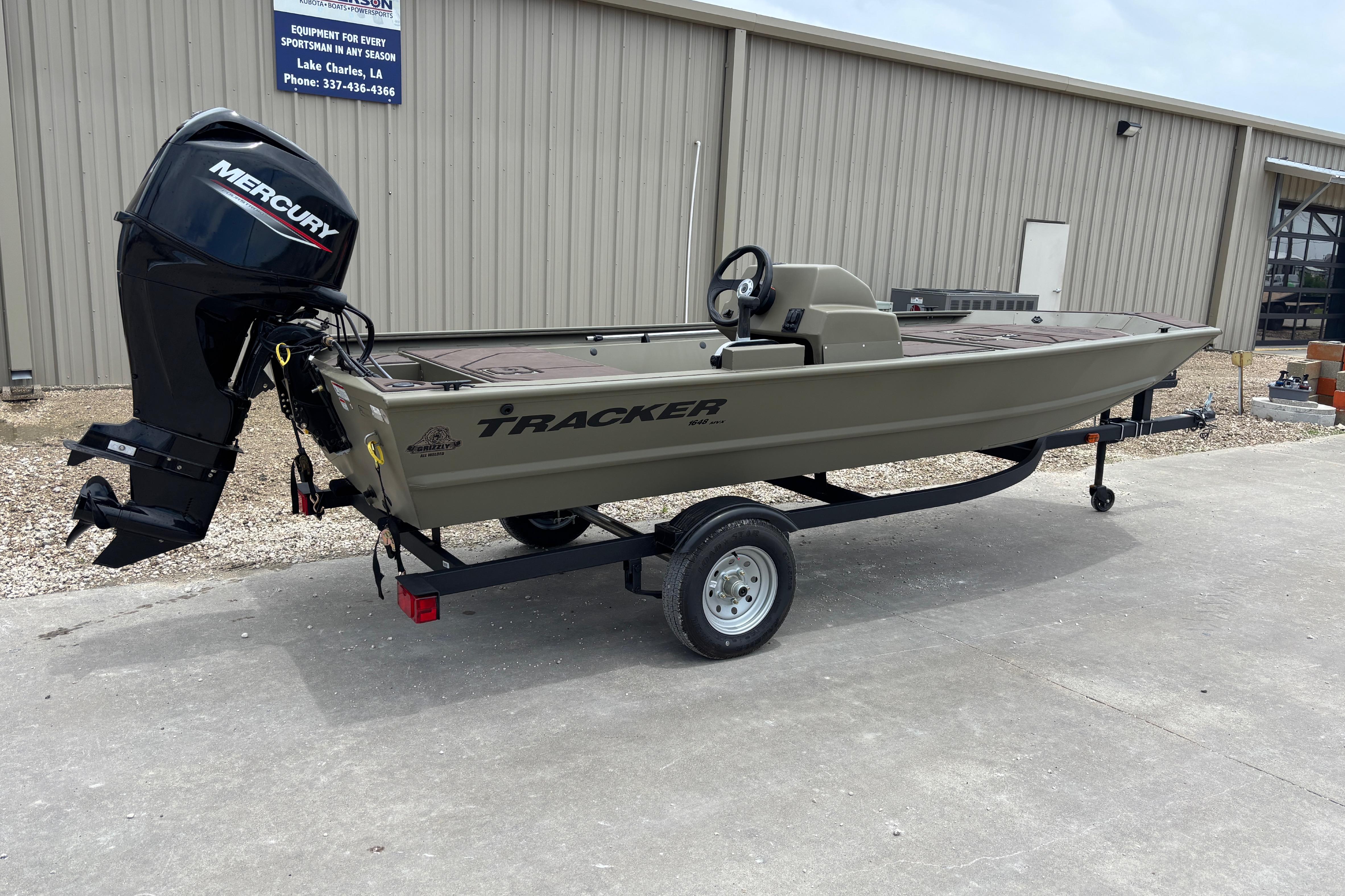 2026 Tracker Grizzly 1648 SC boat with Mercury engine on trailer outside a building.