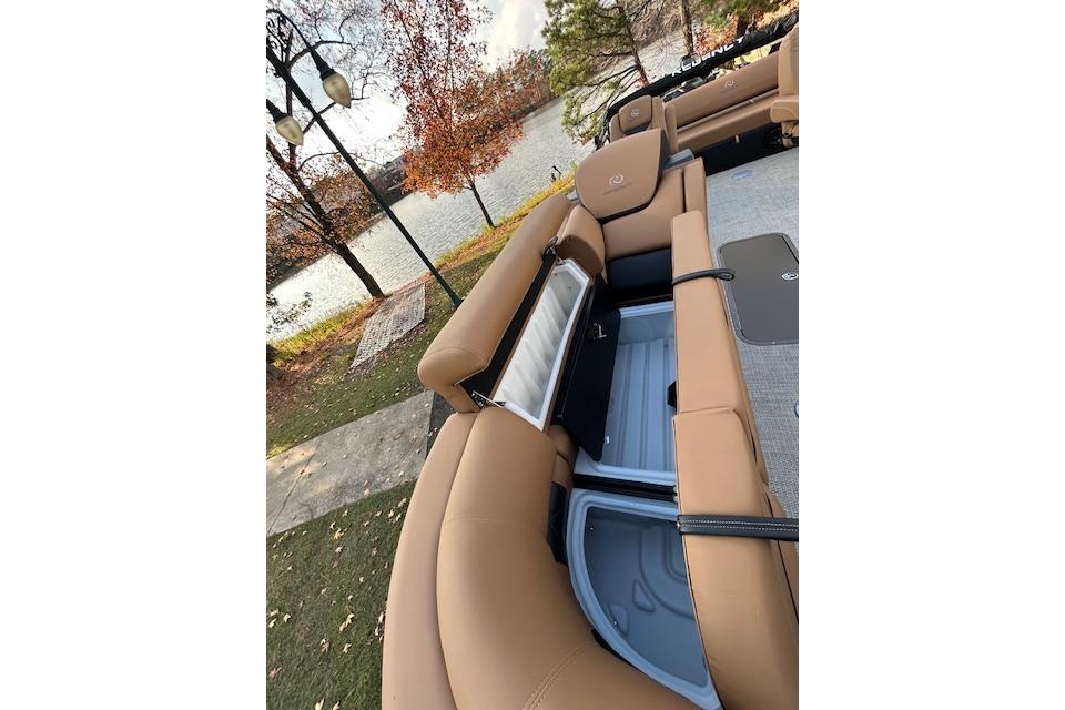 2025 Regency 230 LE3 Sport boat interior with tan seating and storage compartments by a lake.