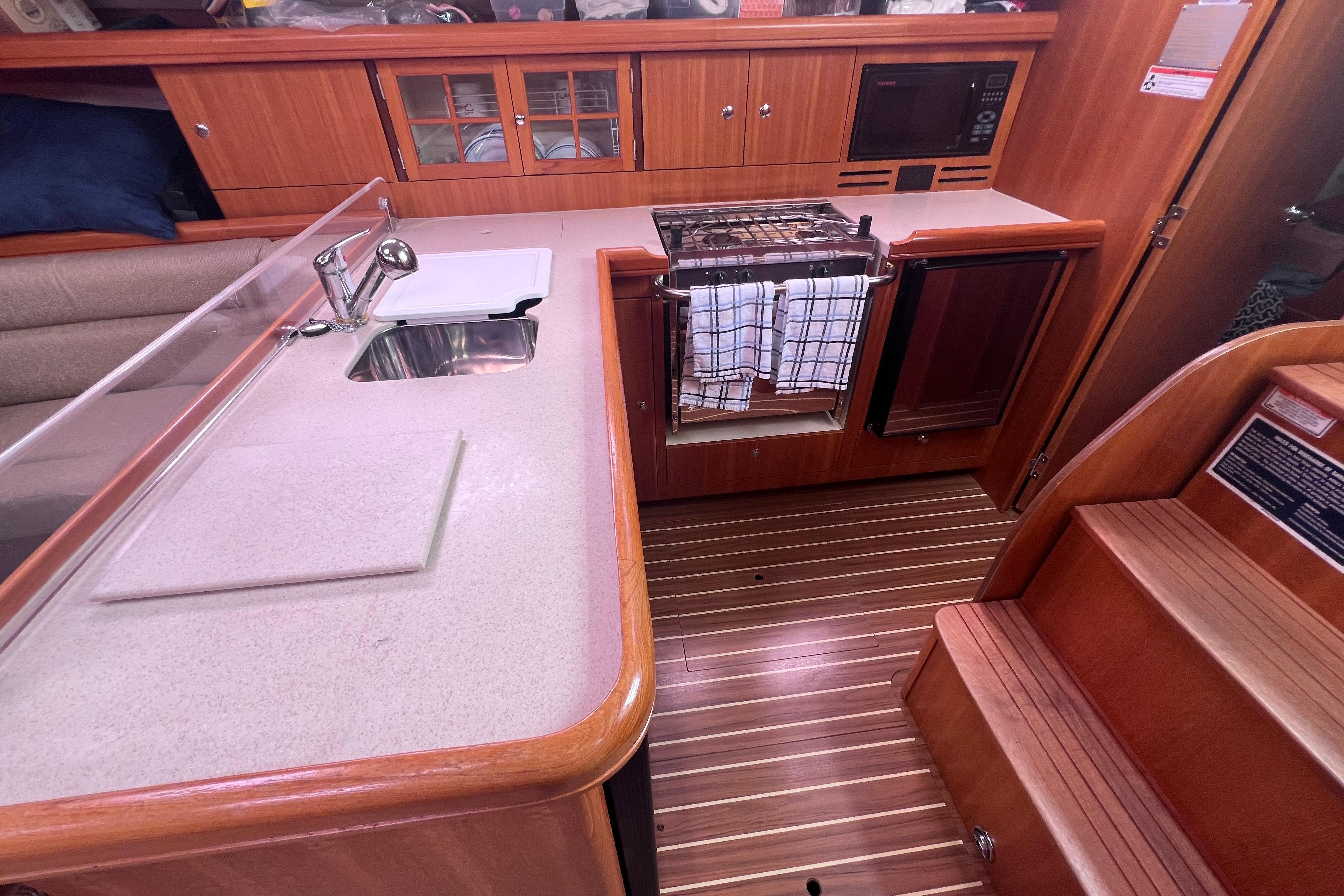Interior of 2006 Hunter 38 sailboat galley with sink, stove, and wooden cabinetry.