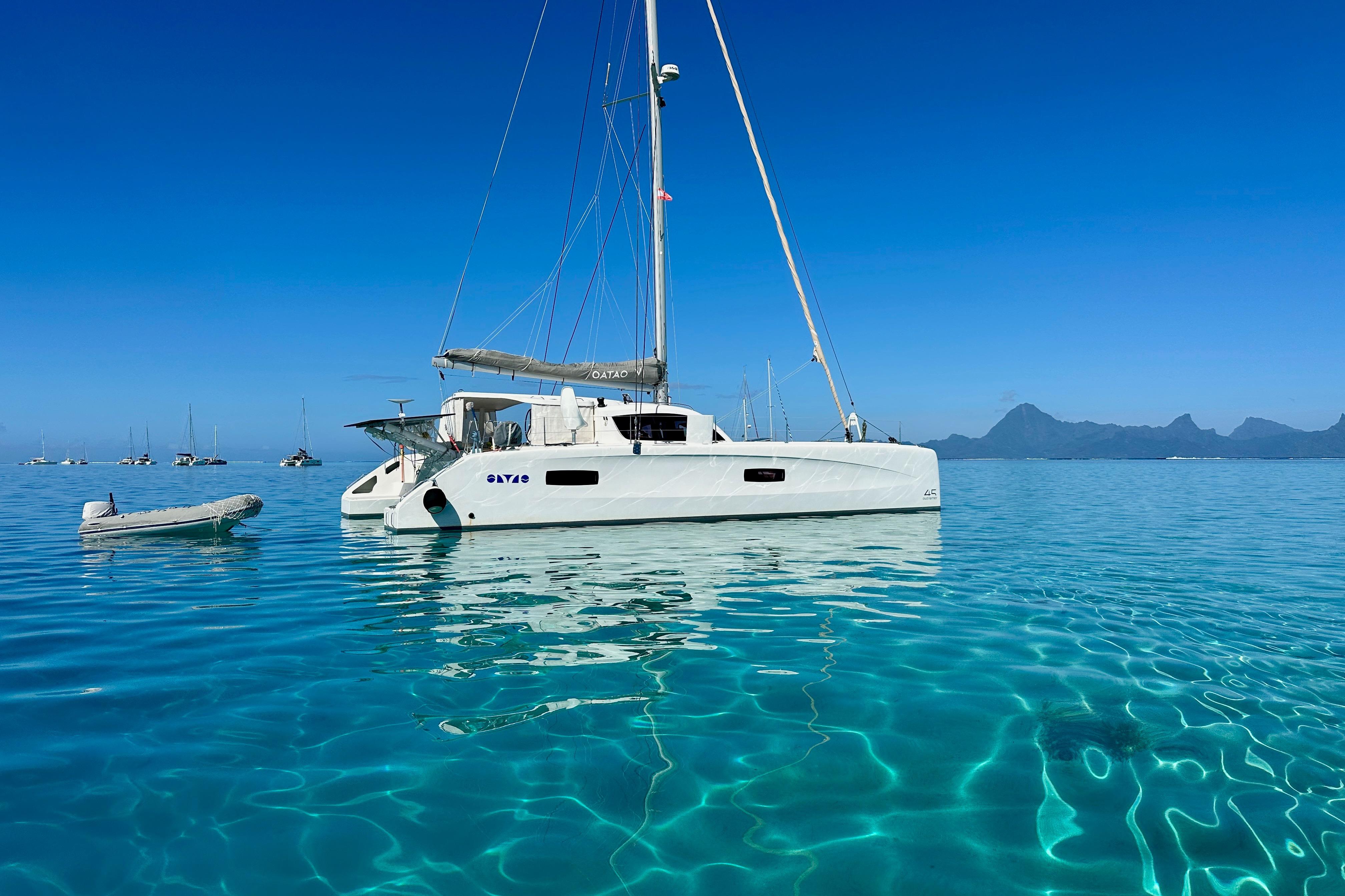2019 Outremer 45 catamaran sailing on clear turquoise waters with mountain backdrop.