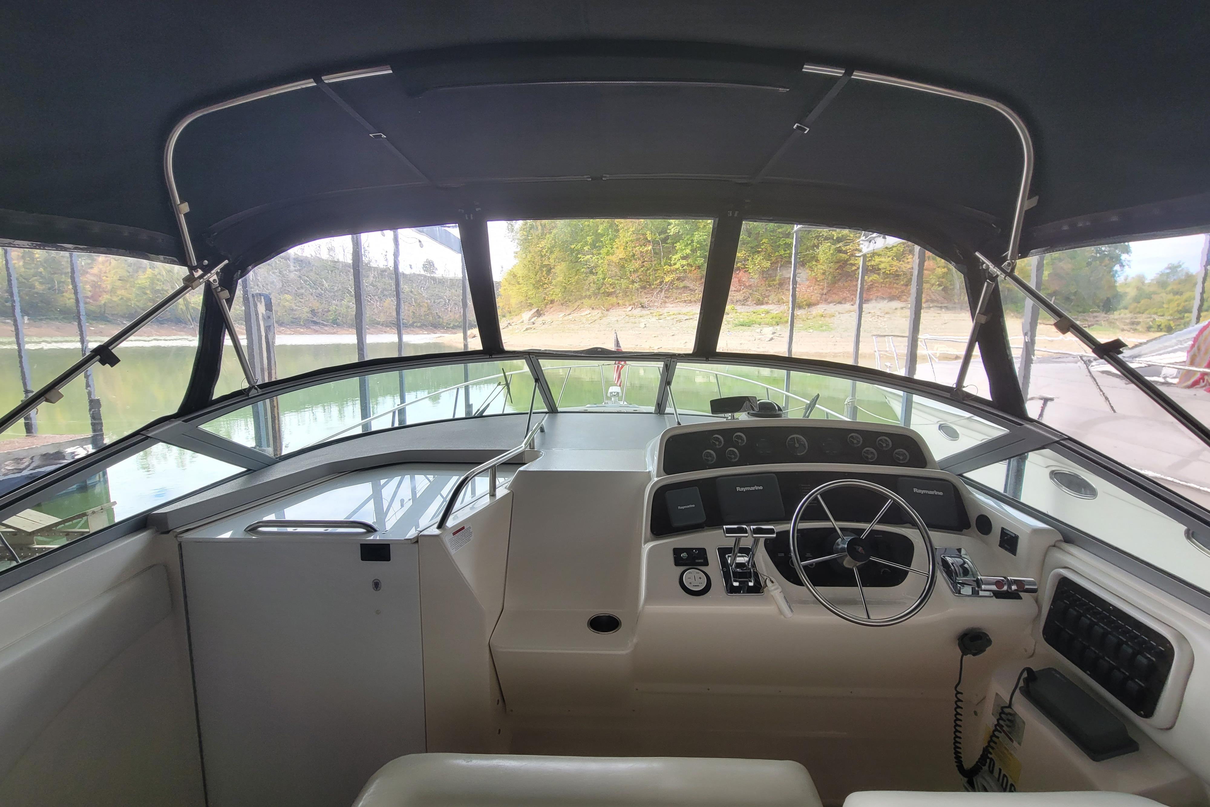 1998 Wellcraft 3200 Martinique boat cockpit with steering wheel and control panel, docked by a serene lake.