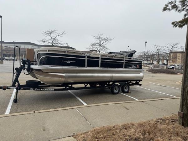 2025 Sun Tracker SportFish 22 DLX pontoon boat on trailer in parking lot.