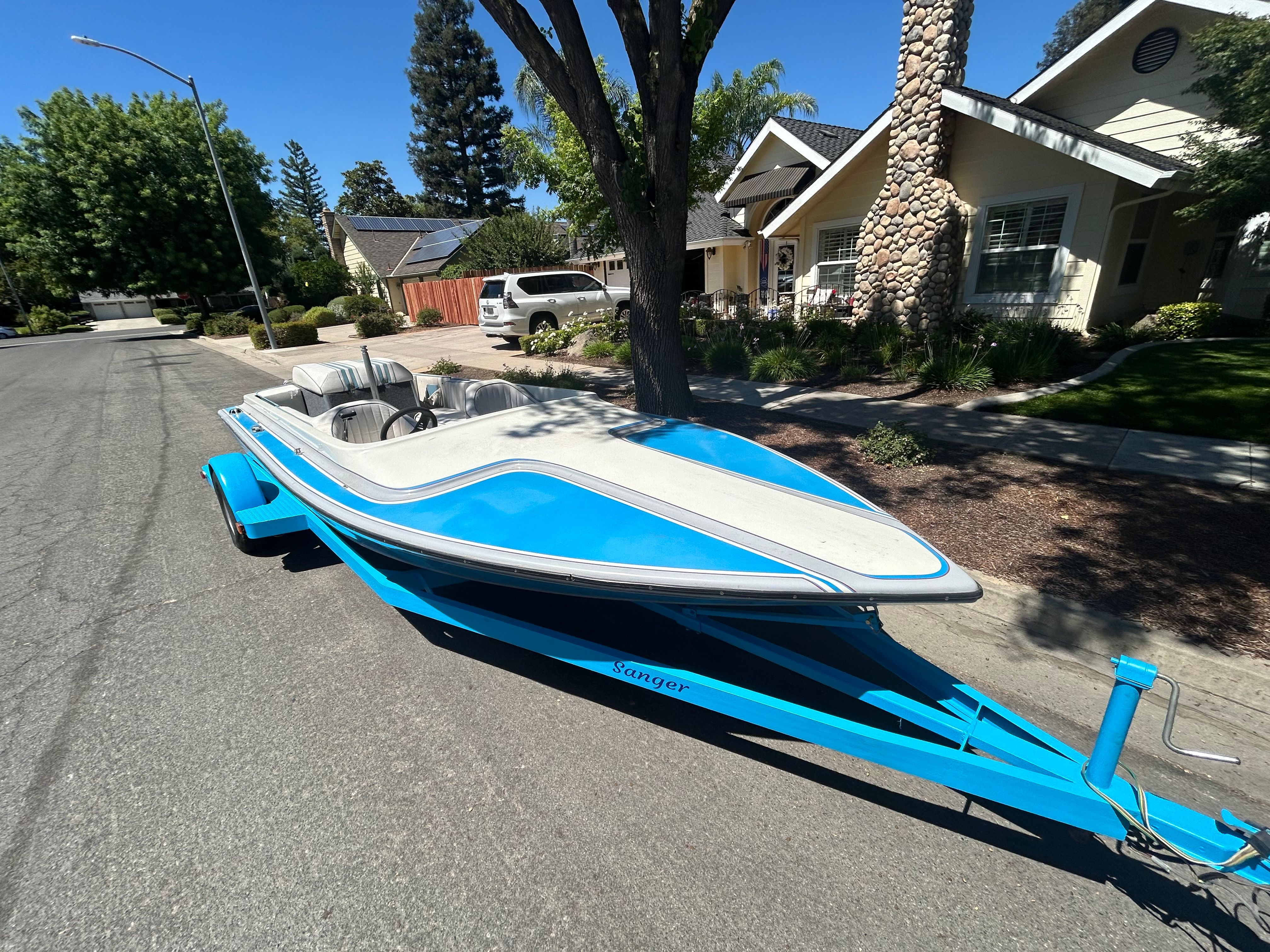 A blue 1988 Sanger Ski Tug on a trailer in a residential street.