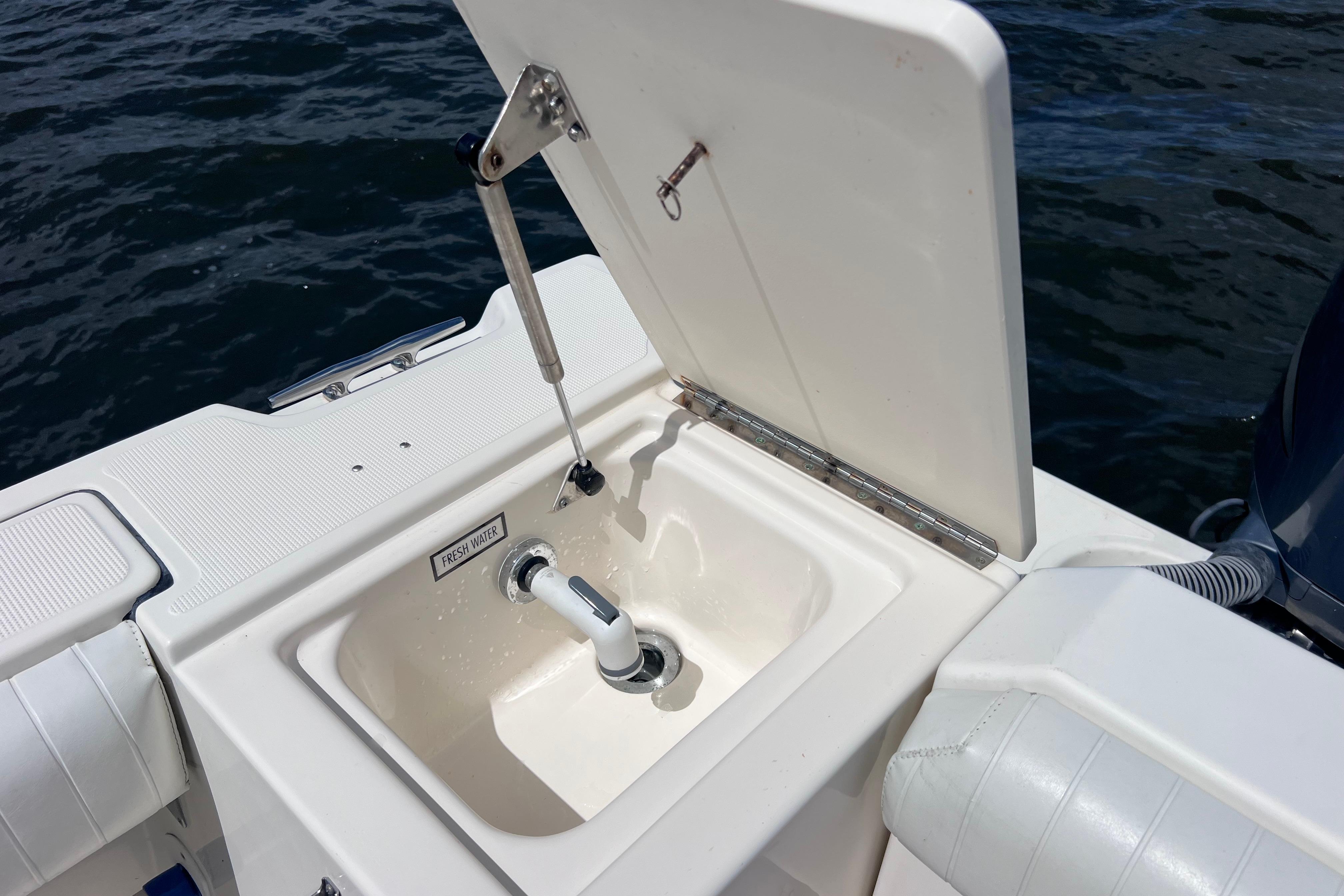 2004 Pursuit 2870 Walkaround boat sink with fresh water tap, open lid, ocean background.
