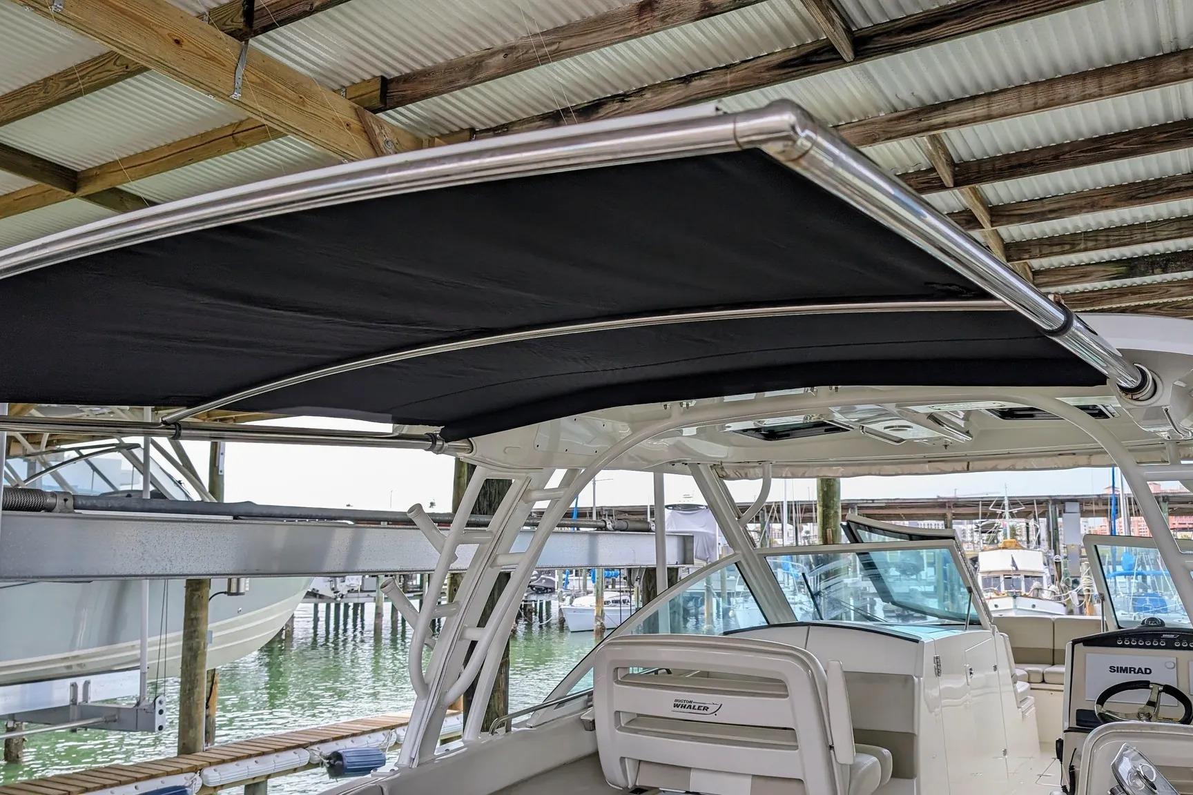 2017 Boston Whaler 320 Vantage boat with black canopy, docked under a wooden roof.