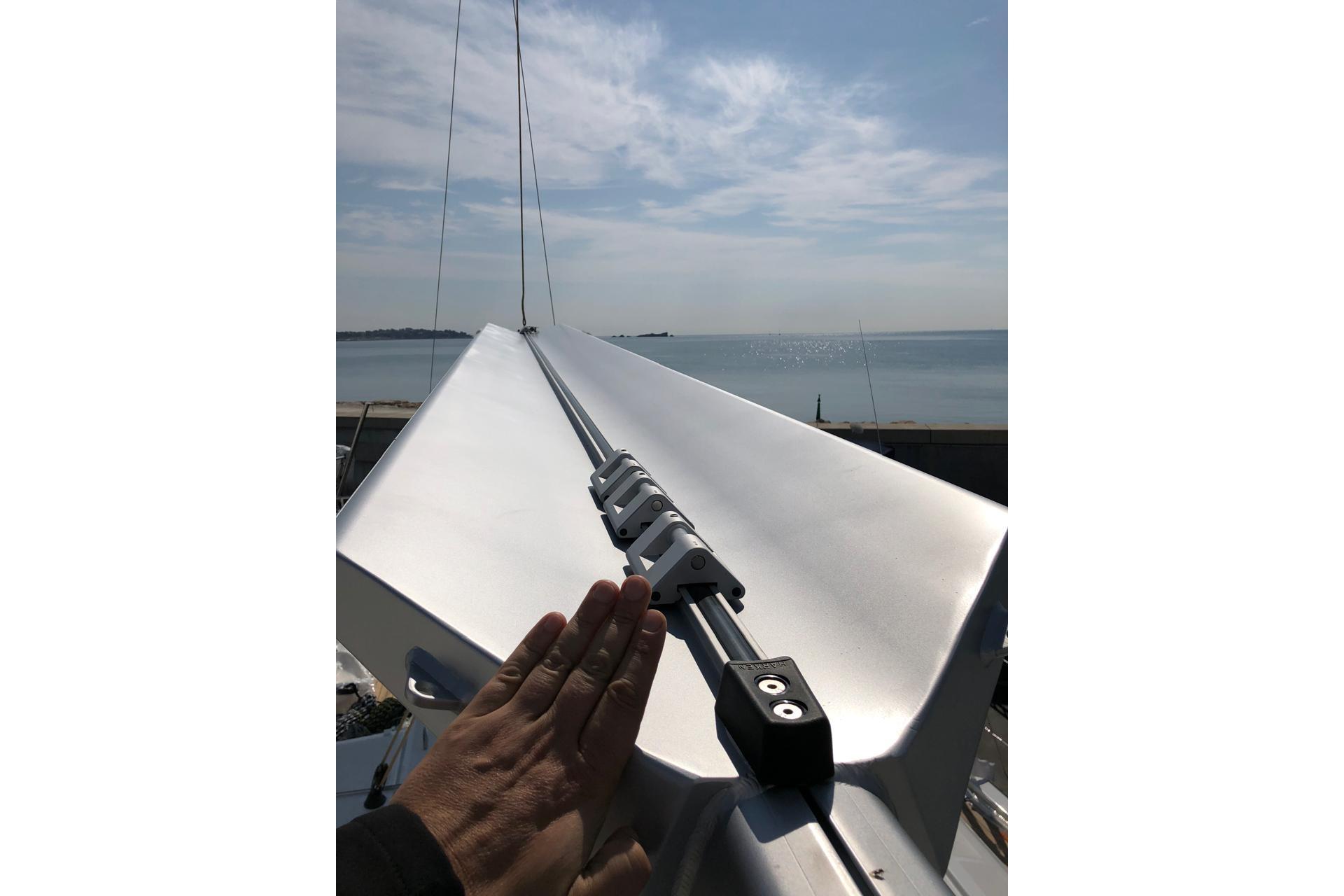 Hand on Jeanneau 54 sailboat mast, 2018 model, with ocean view in background.