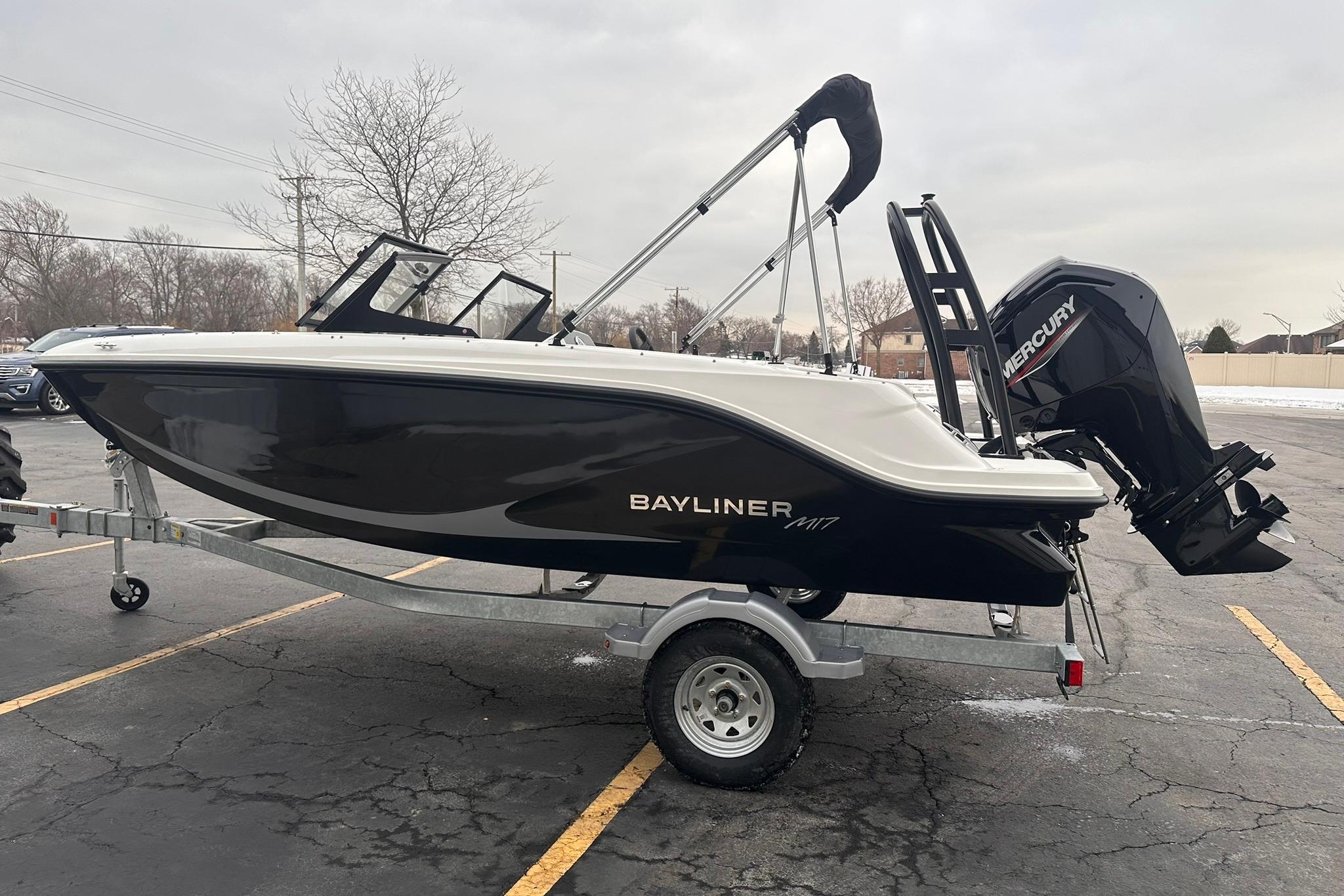 2026 Bayliner M17 boat on trailer with Mercury outboard motor in parking lot.