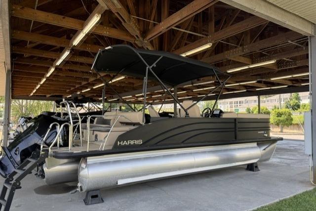 2025 Harris Sunliner 230 pontoon boat under wooden shelter, featuring sleek design and modern amenities.