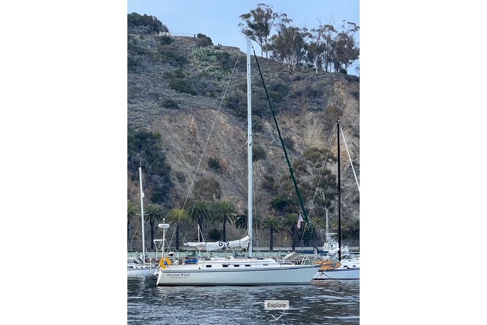 Sailboat Caliber 33, 1991 model, anchored near a rocky hillside with palm trees.