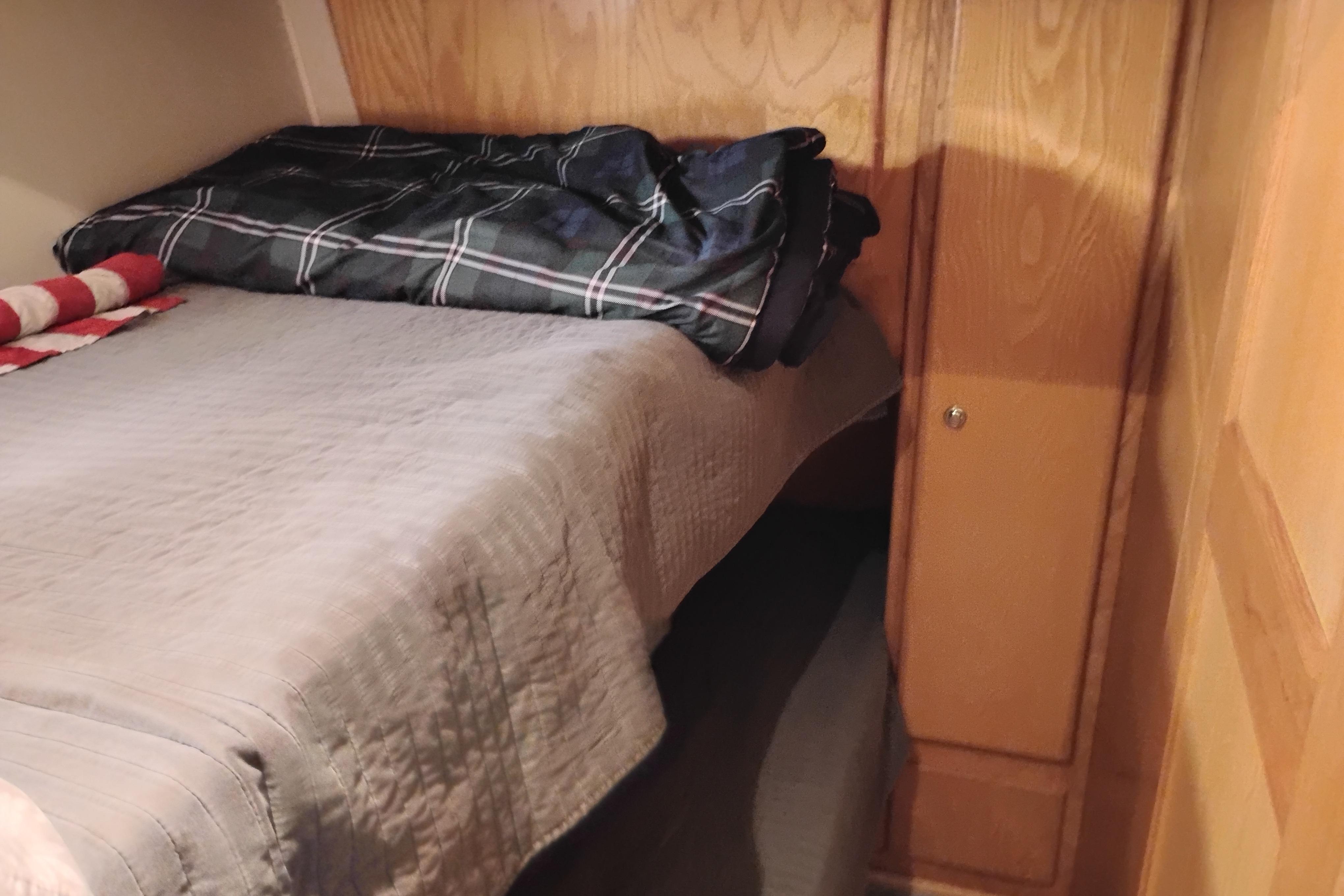 Cozy bed in 1994 Navigator Classic RV with wooden cabinetry and plaid bedding.