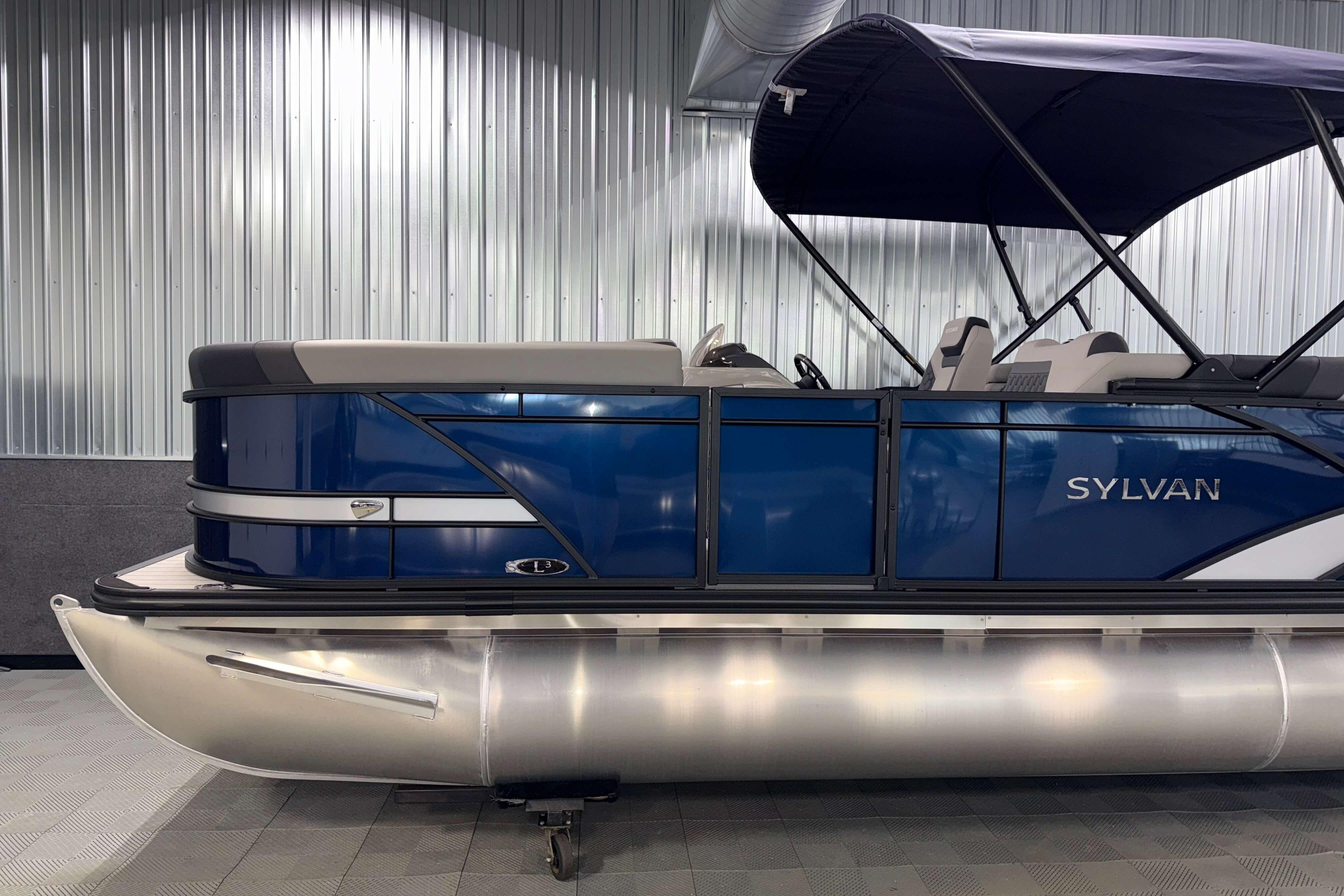 2026 Sylvan L3 SLZ pontoon boat with blue exterior and canopy in showroom.