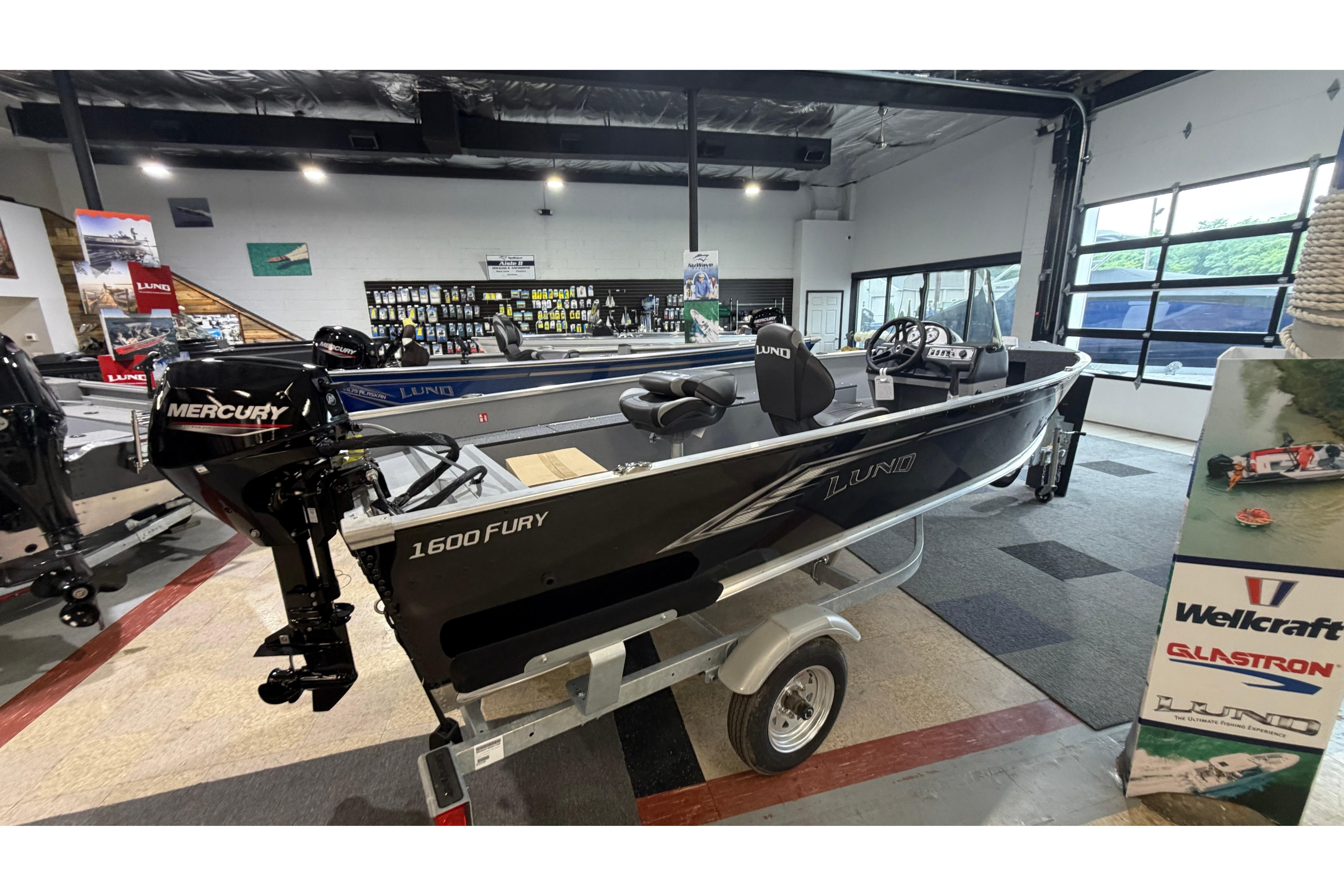 2027 Lund 1600 Fury SS fishing boat displayed in showroom with Mercury outboard motor.