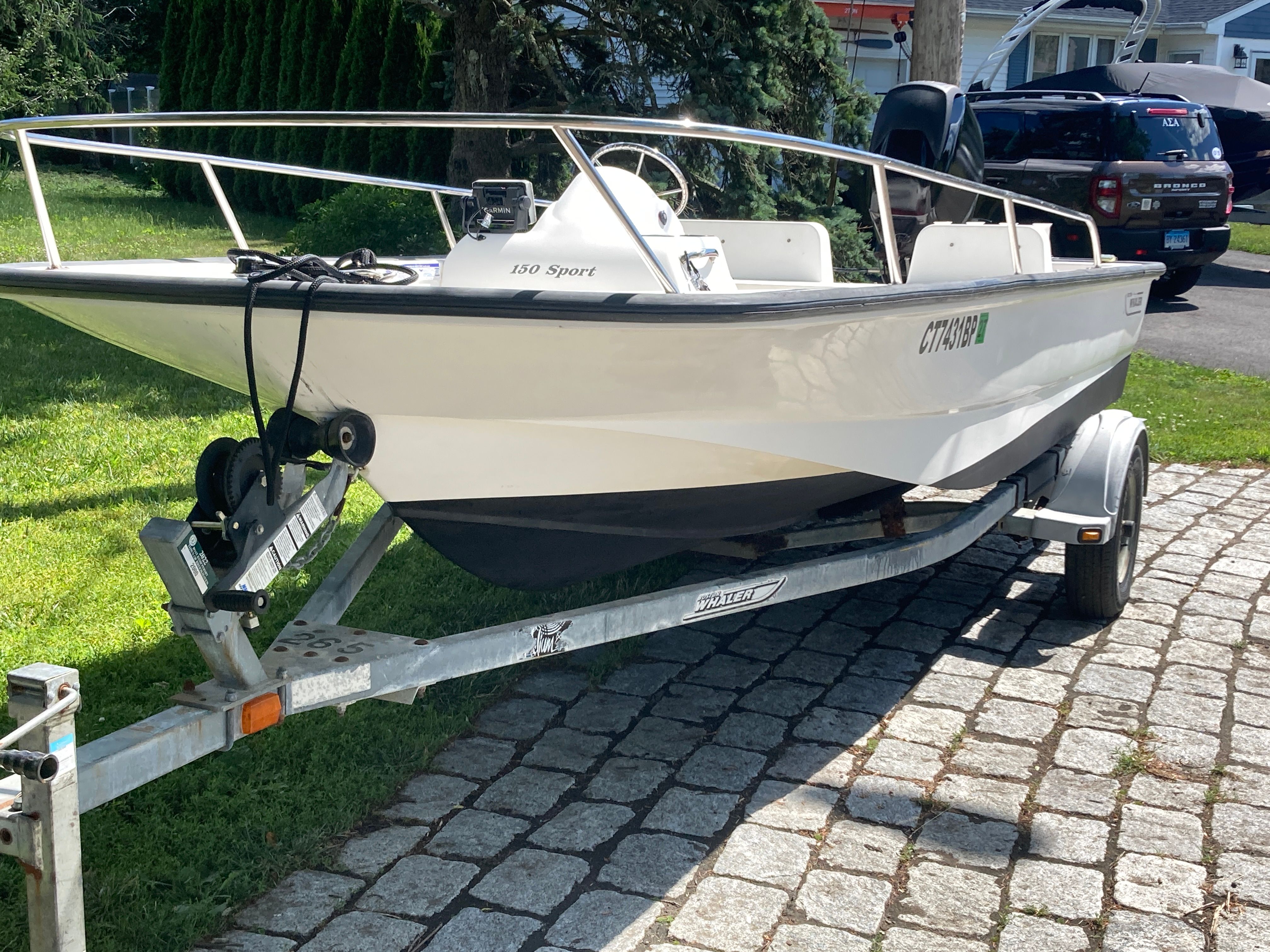 A 2004 Boston Whaler 150 Sport on a trailer, parked on a cobblestone driveway.