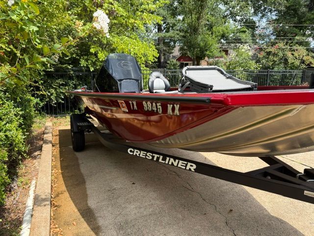 A red Crestliner XF 179 boat from 2024 on a trailer in a garden setting.