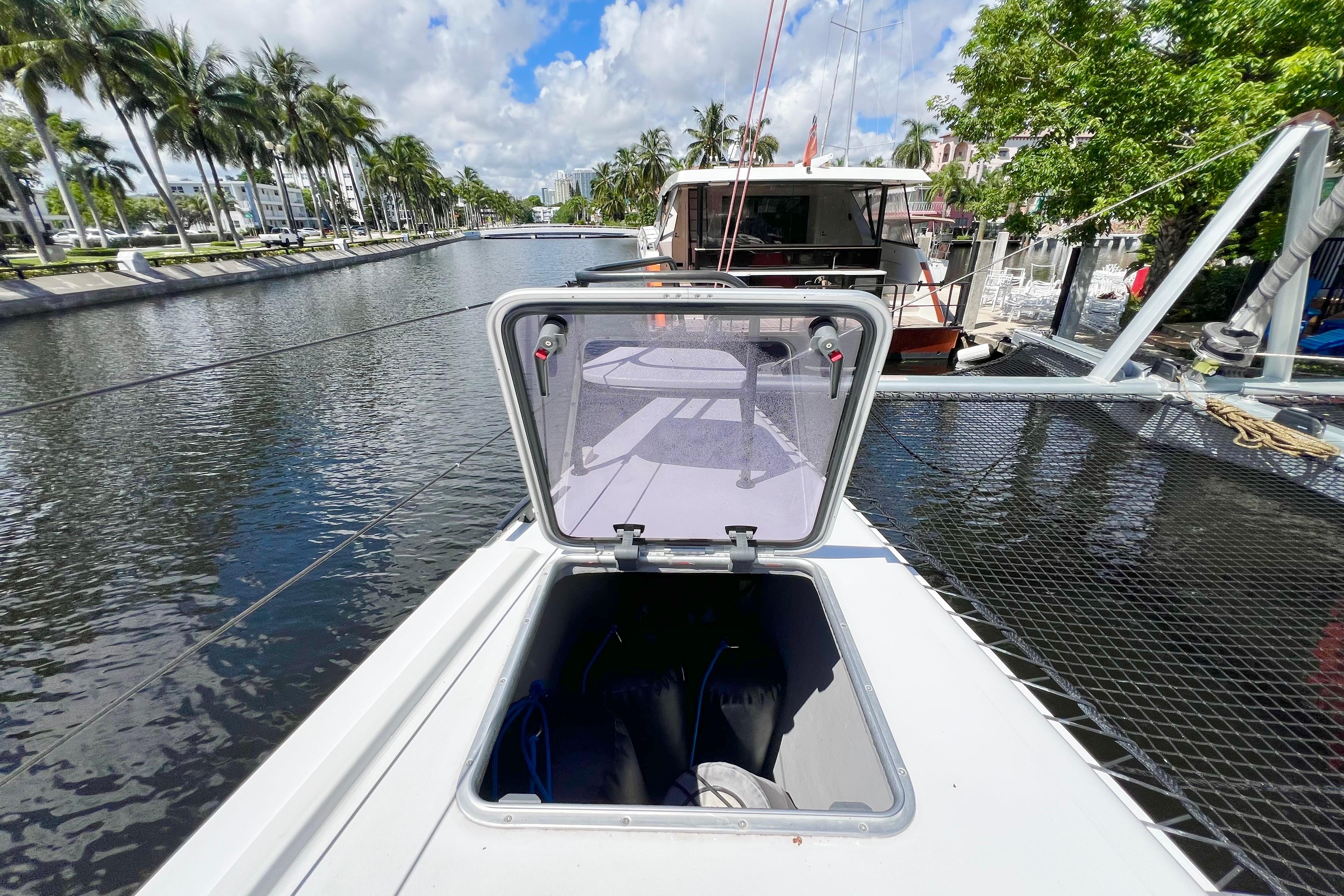 Sailboat deck with open hatch, Balance 482 model, docked by a palm-lined canal.