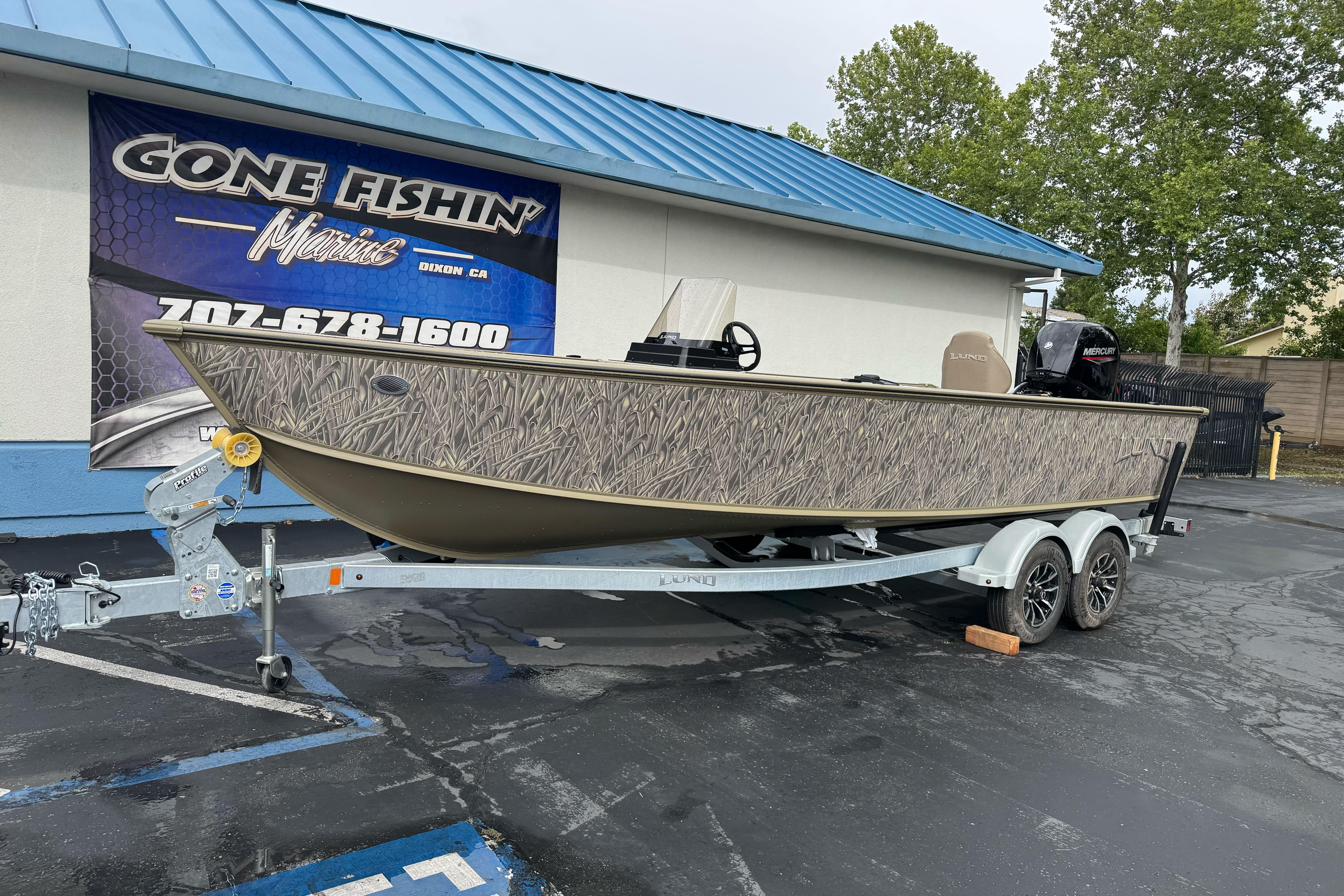 2026 Lund 2075 Alaskan SS boat on trailer at dealership, featuring camouflage design.