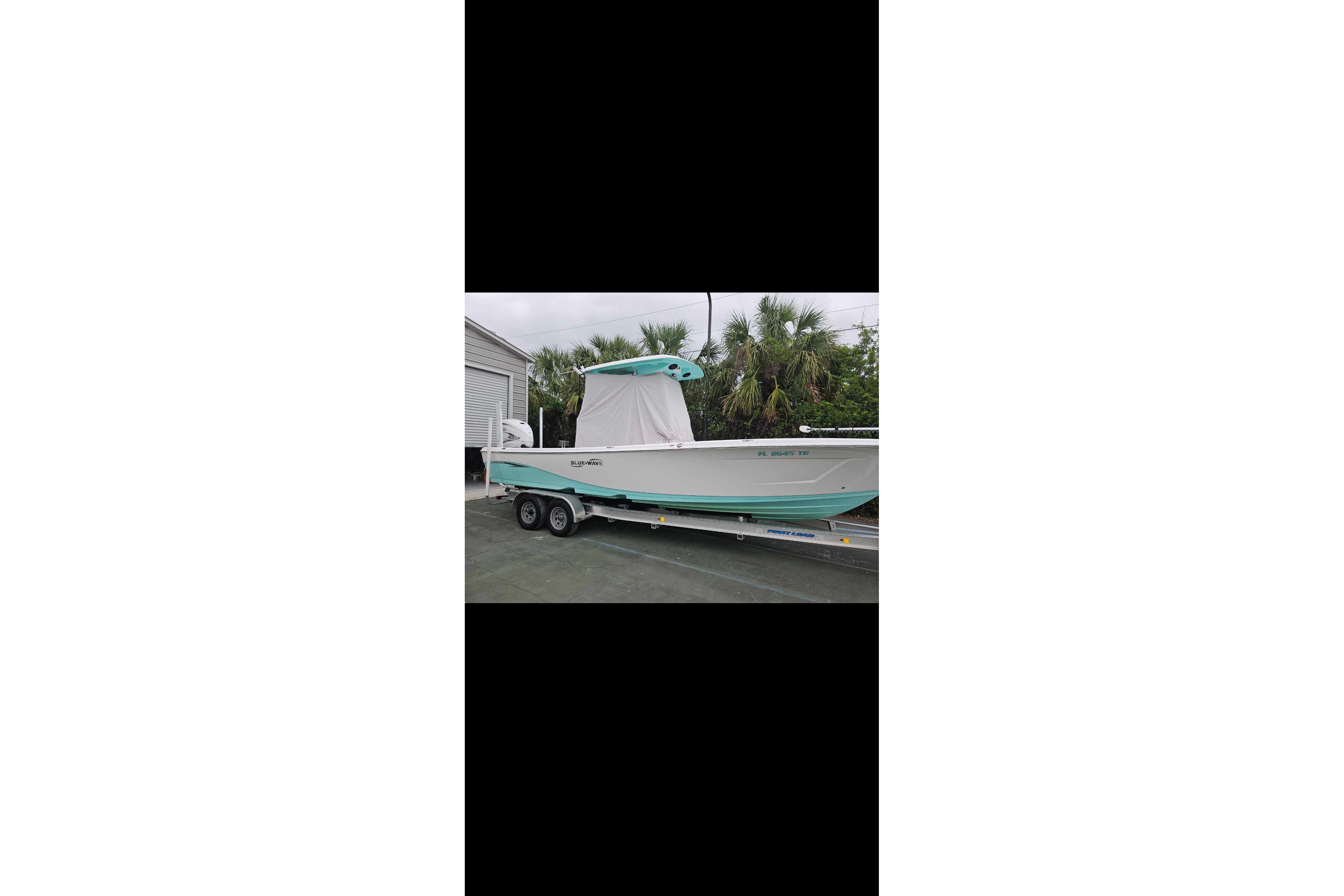 2022 Blue Wave 2800 Pure Hybrid boat on trailer, parked near palm trees.