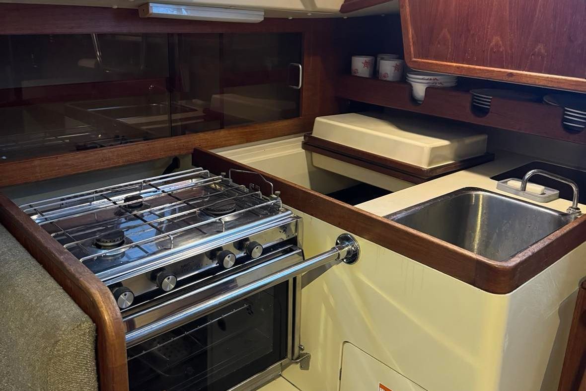 Small kitchen in a boat with stove, sink, and wooden cabinets.