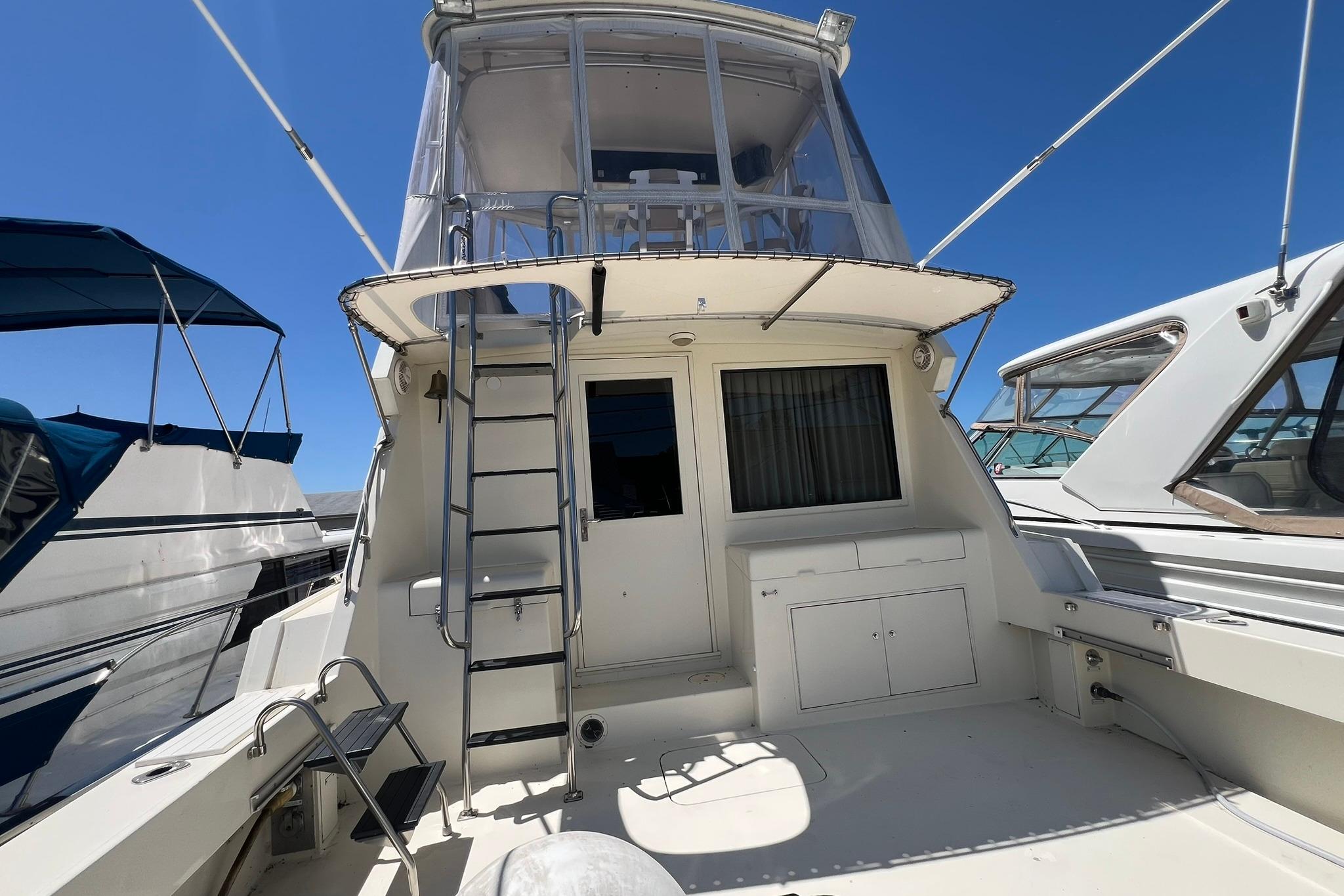1990 Hatteras 41 Convertible yacht with upper deck and ladder, docked under clear blue sky.