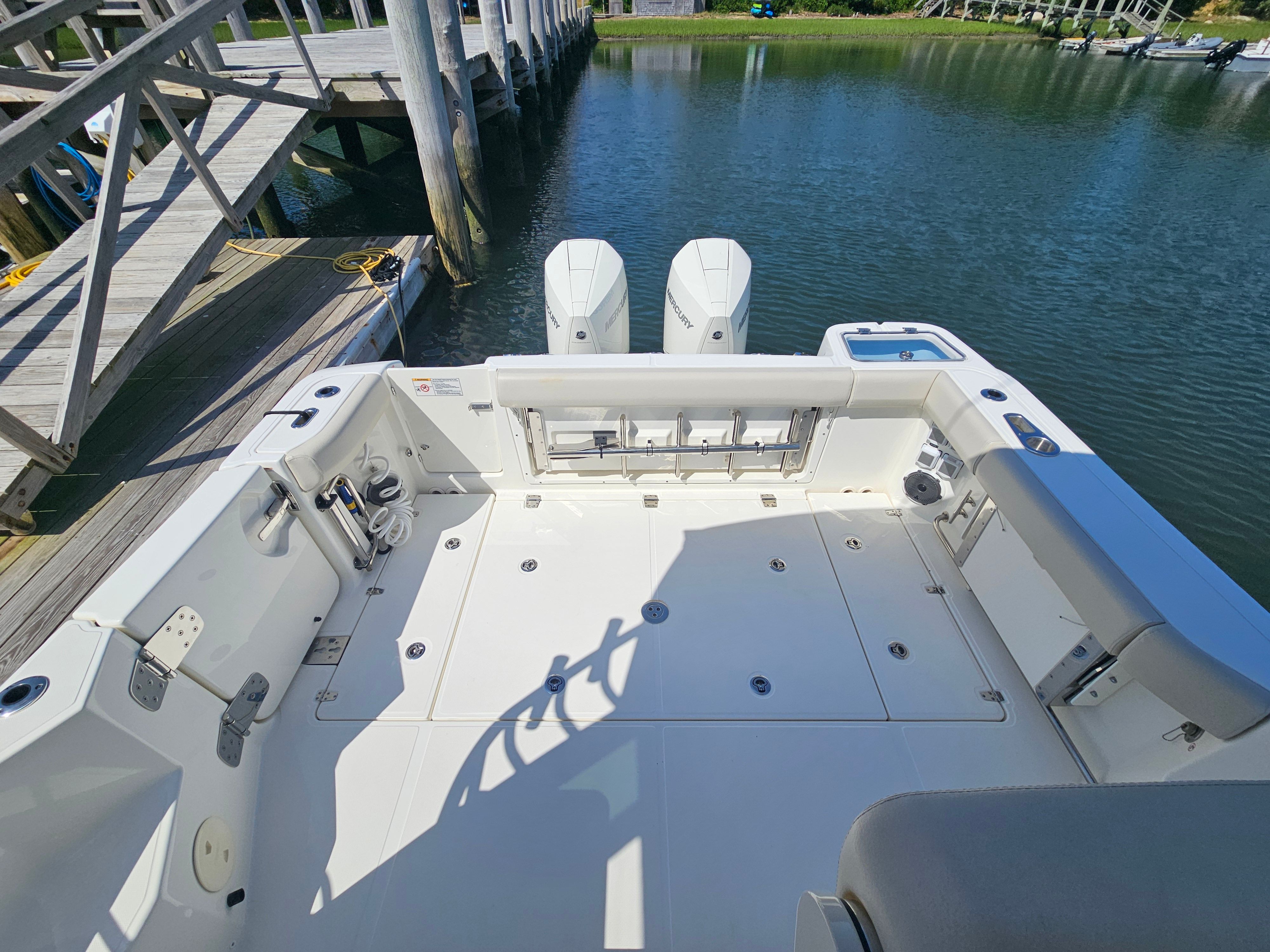 The image shows the spacious aft deck of a 2023 Boston Whaler 325 Conquest, docked by a pier.