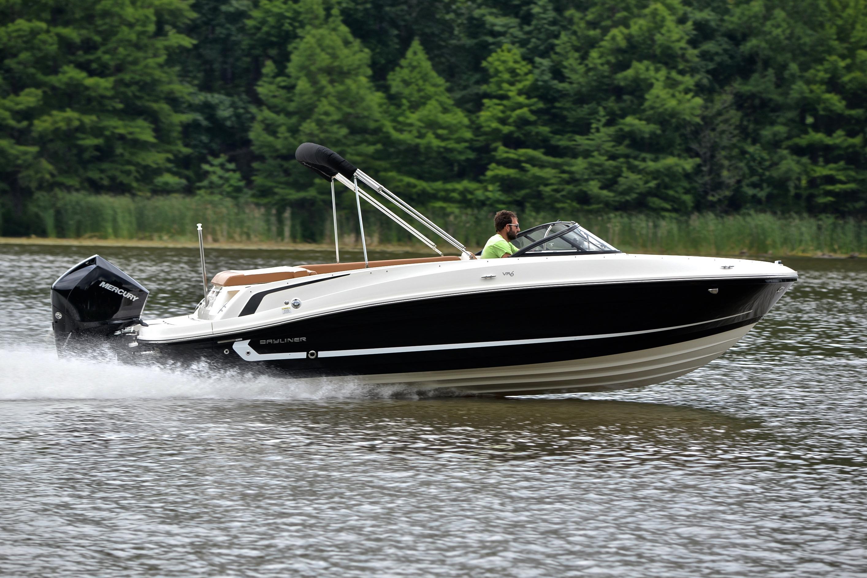 2019 Bayliner VR6 Bowrider OB cruising on a lake with lush green forest backdrop.