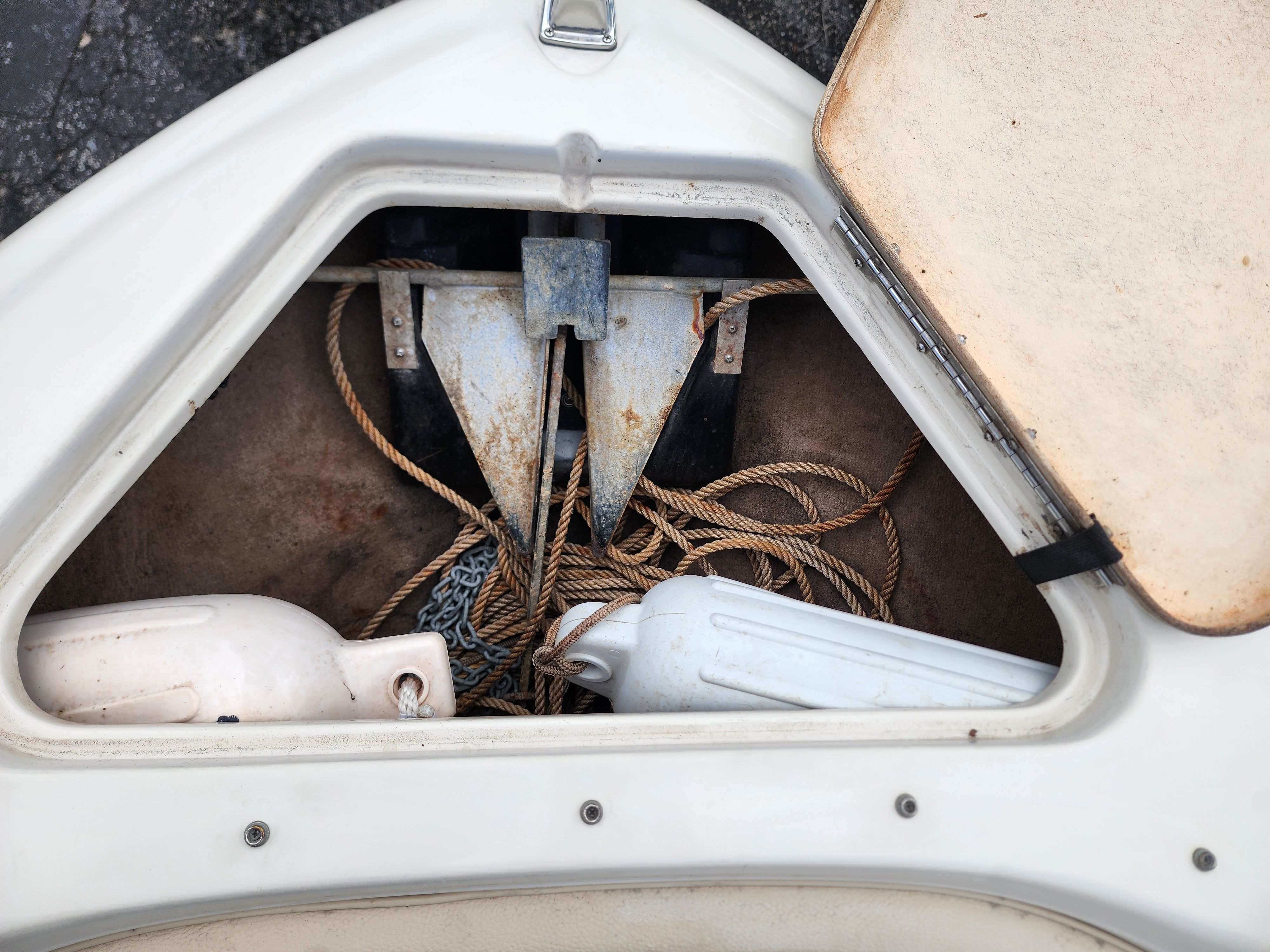 An open storage compartment with anchor, ropes, and fenders on a boat.