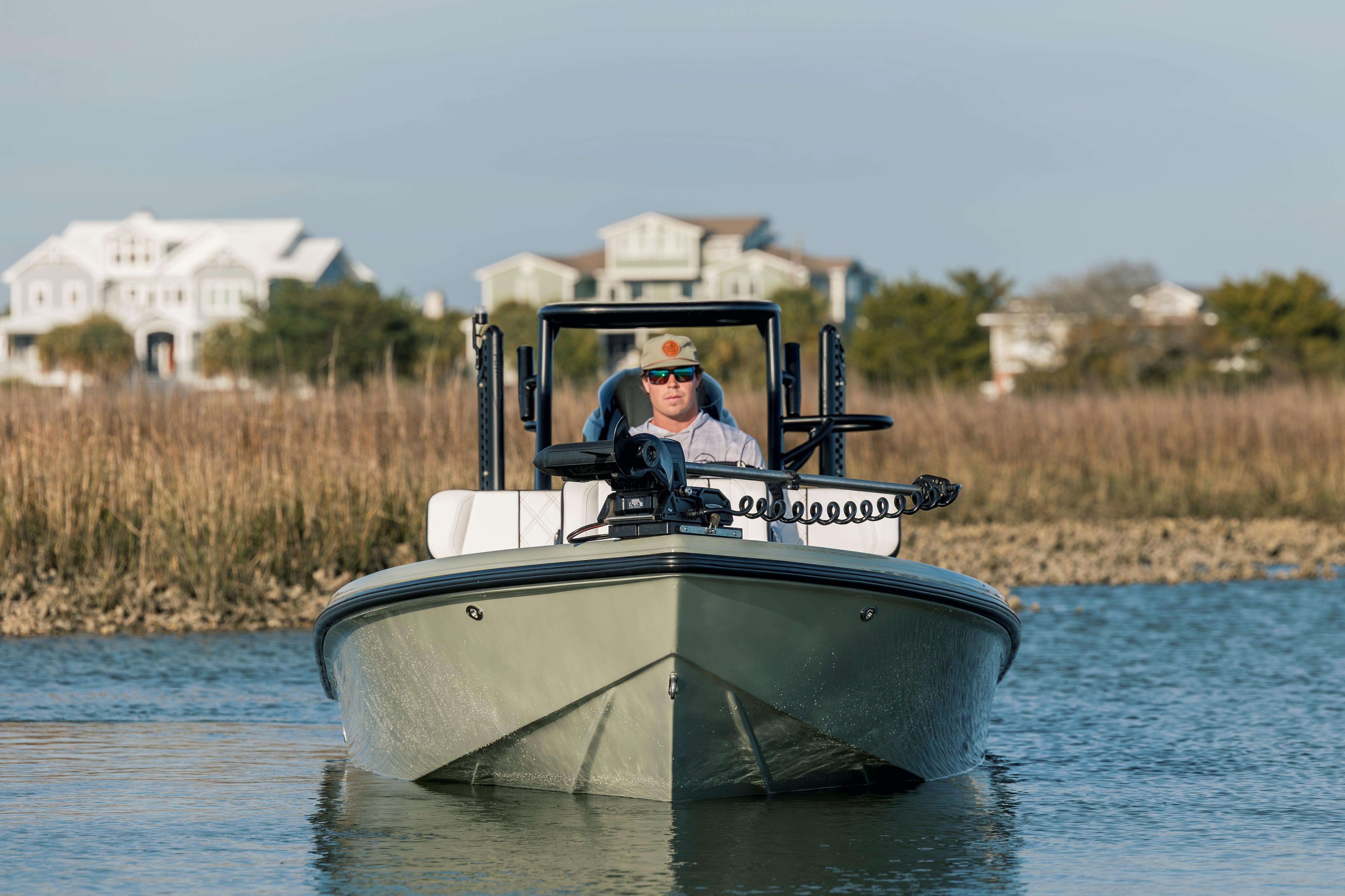 Man piloting a 2025 Vtech 18 boat on a calm waterway near coastal homes.