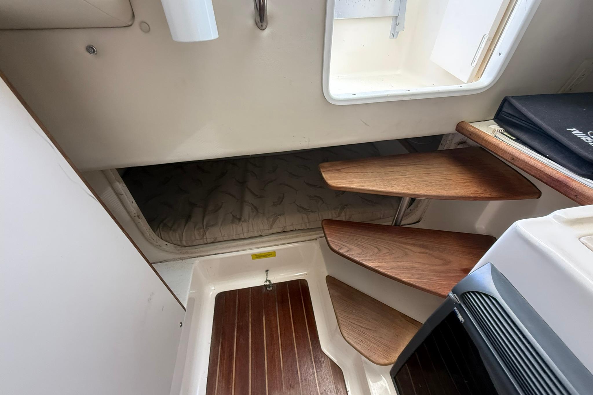 Interior cabin of 2003 Pursuit 2870 Walkaround with wooden steps and cozy sleeping area.