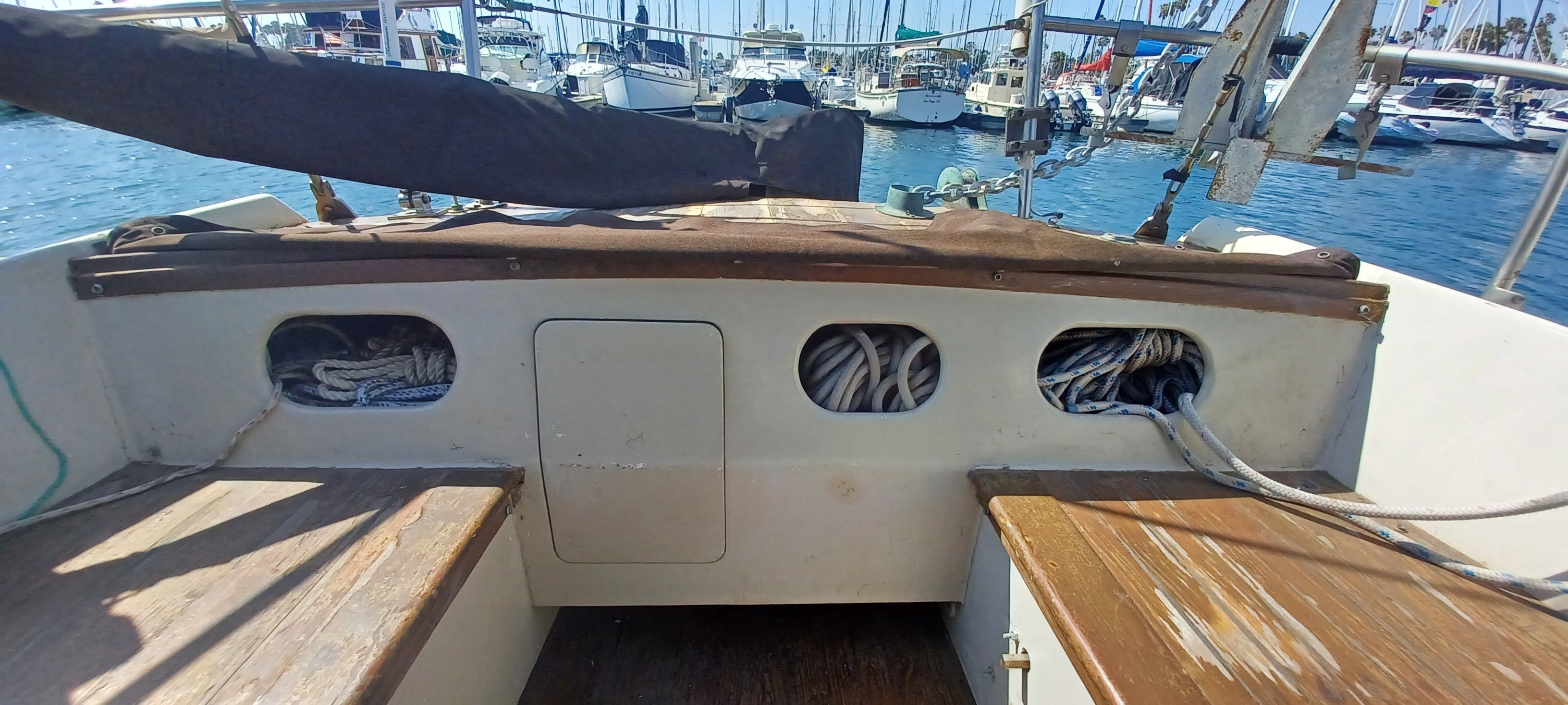 The cockpit of a sailboat with ropes and wooden benches in a marina.