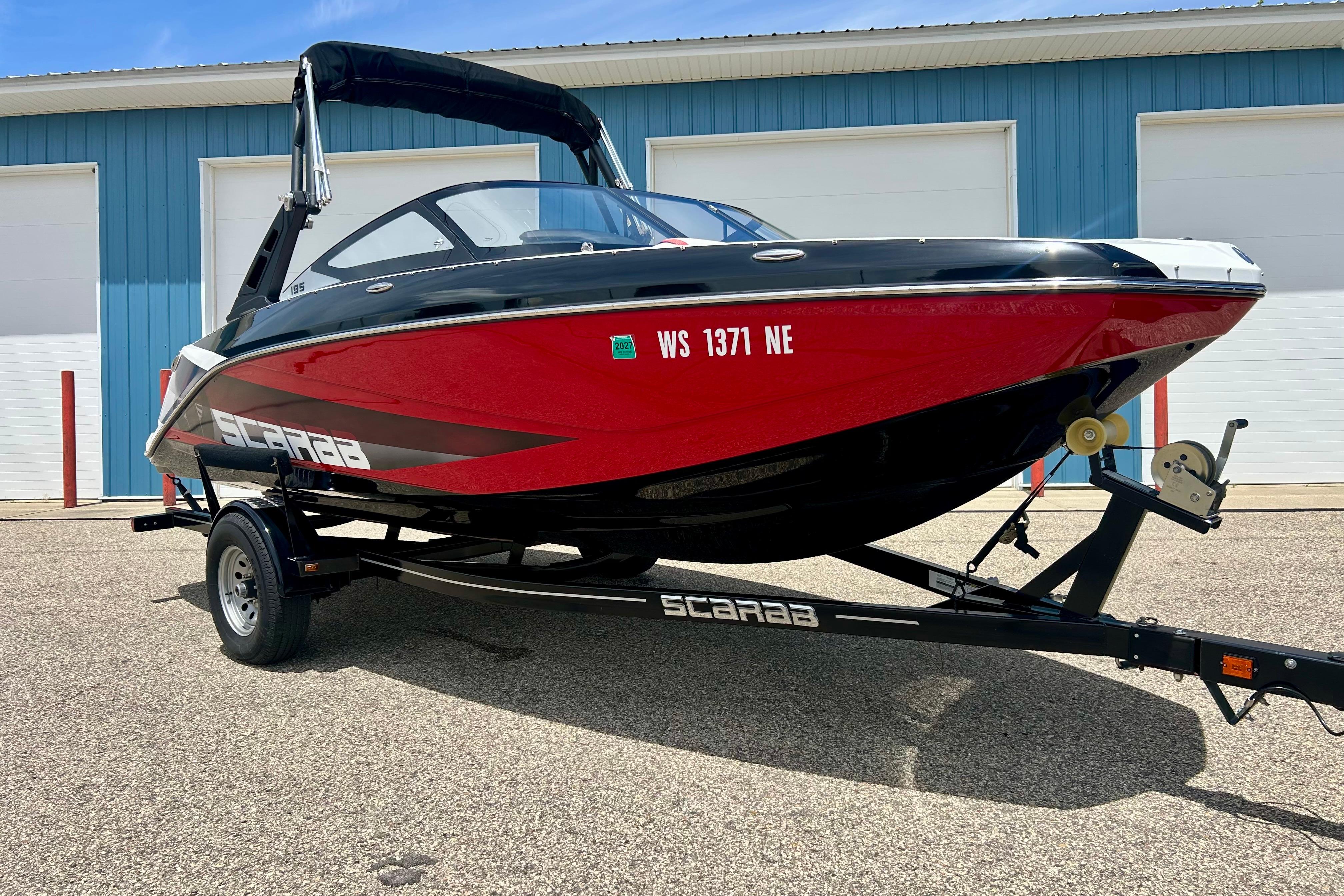 2021 Scarab 195 ID boat on trailer, red and black design, parked outside a blue building.
