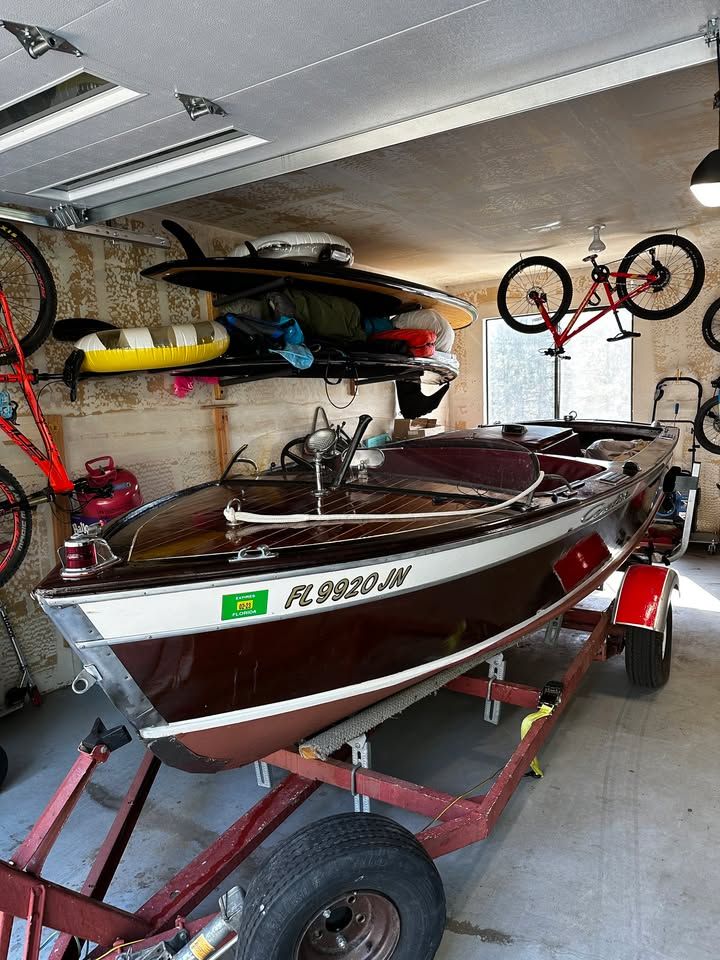 A 1957 Chris-Craft CAVALIER on a trailer in a garage, surrounded by bikes and gear.