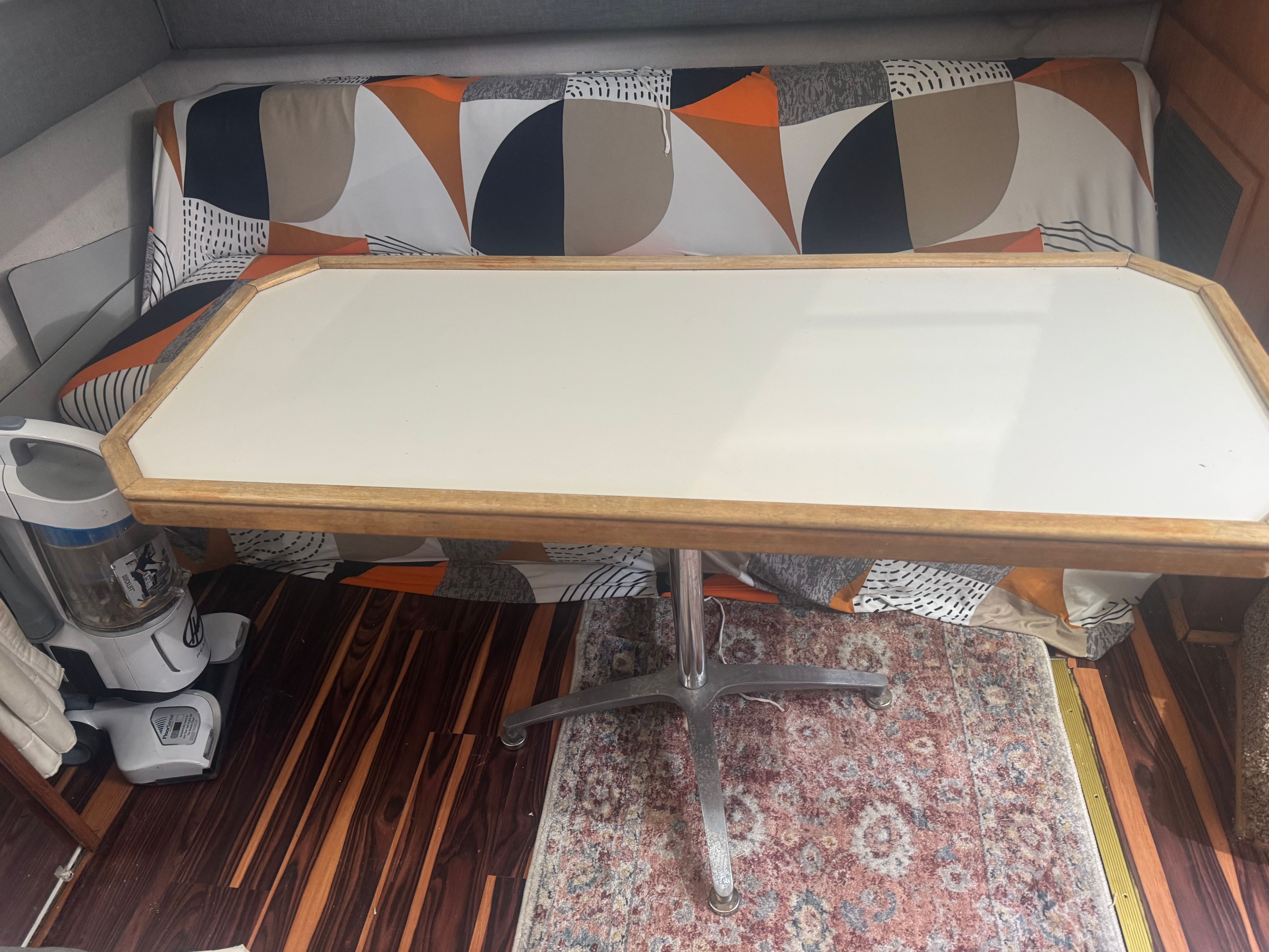 A table with a wooden frame stands in front of a patterned couch on a boat.