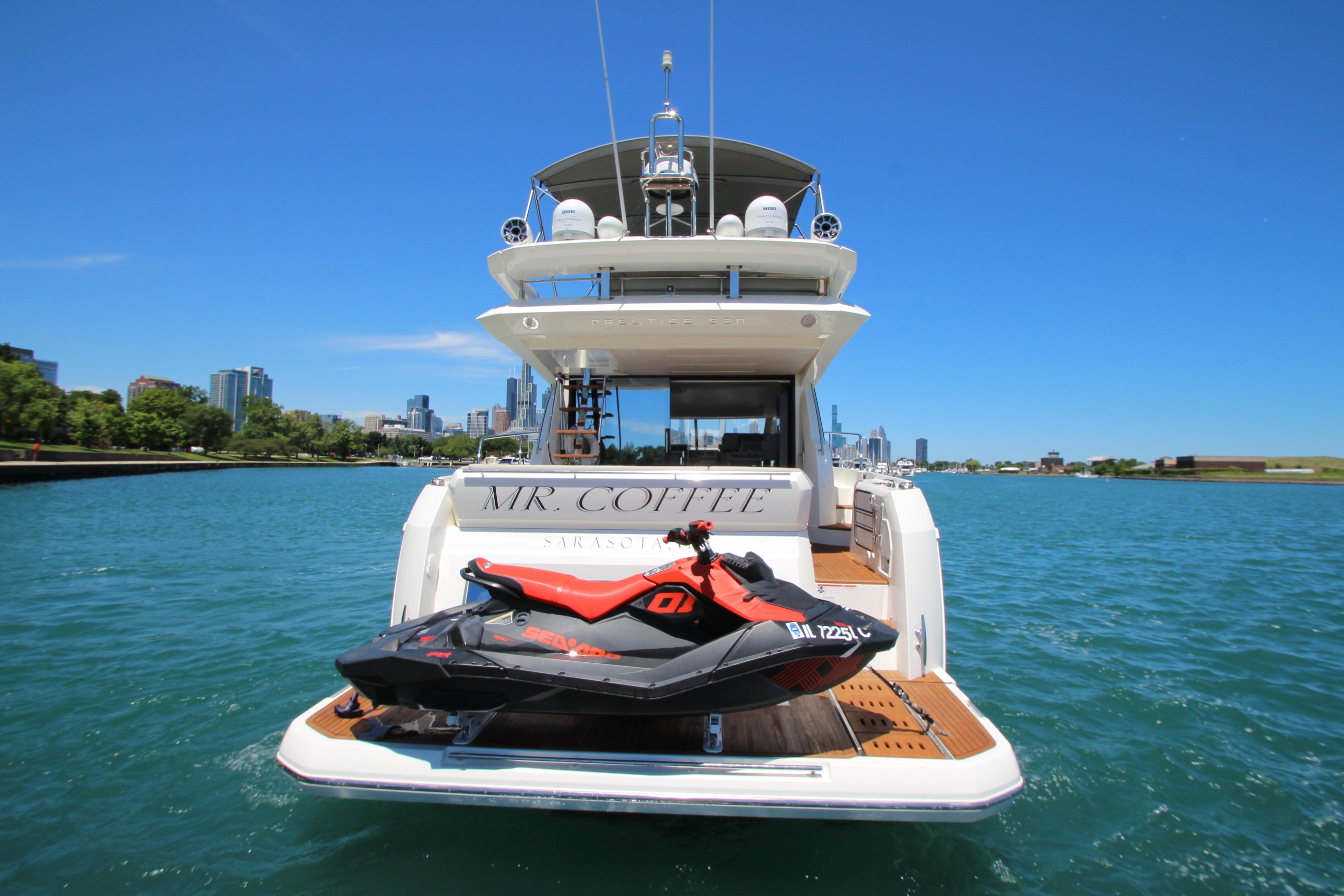 Luxury 2022 Prestige 520 yacht with jet ski on deck, cruising near city skyline.
