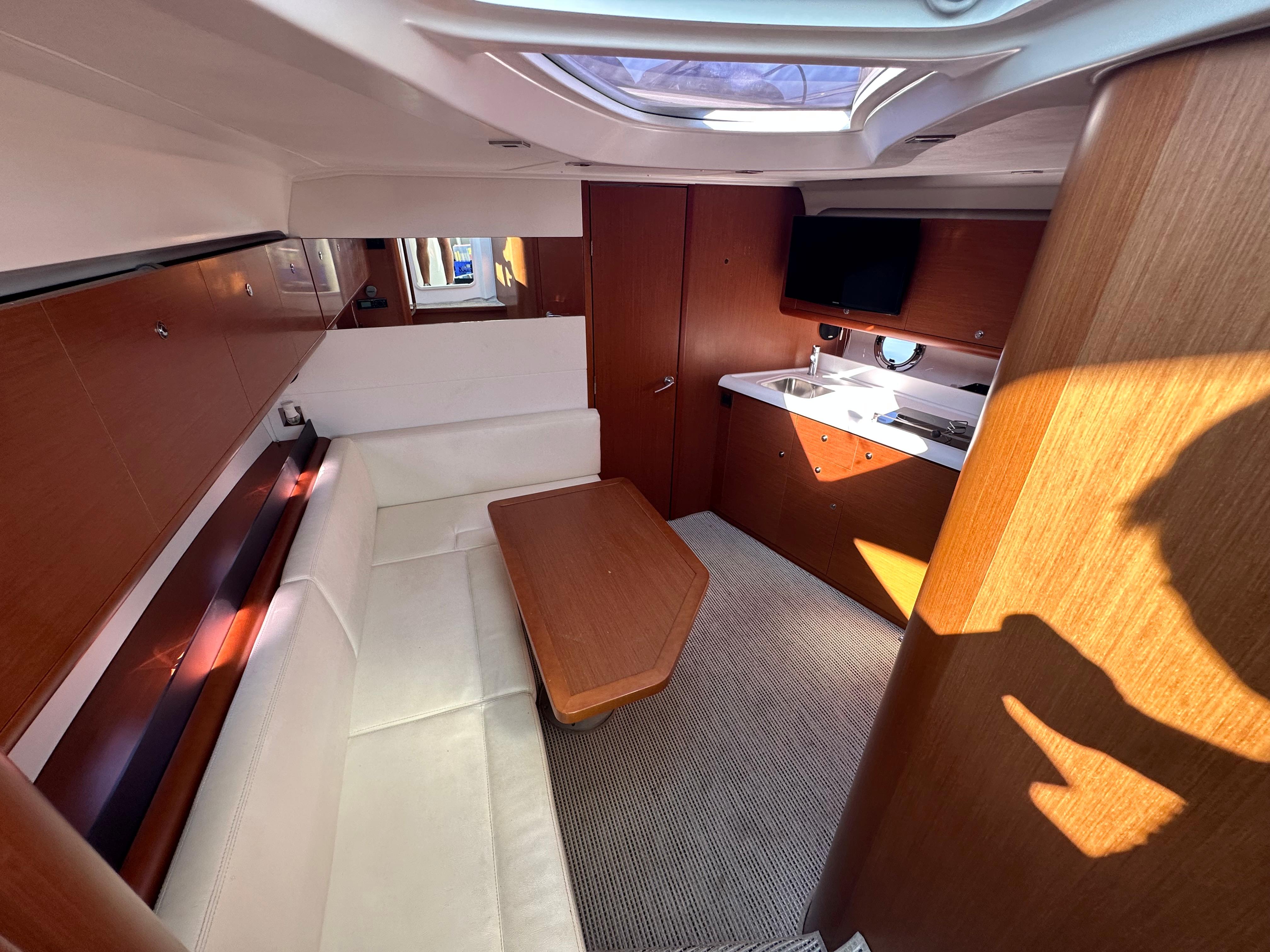 2013 Beneteau Gran Turismo 38 interior with white seating, wooden table, and kitchenette.