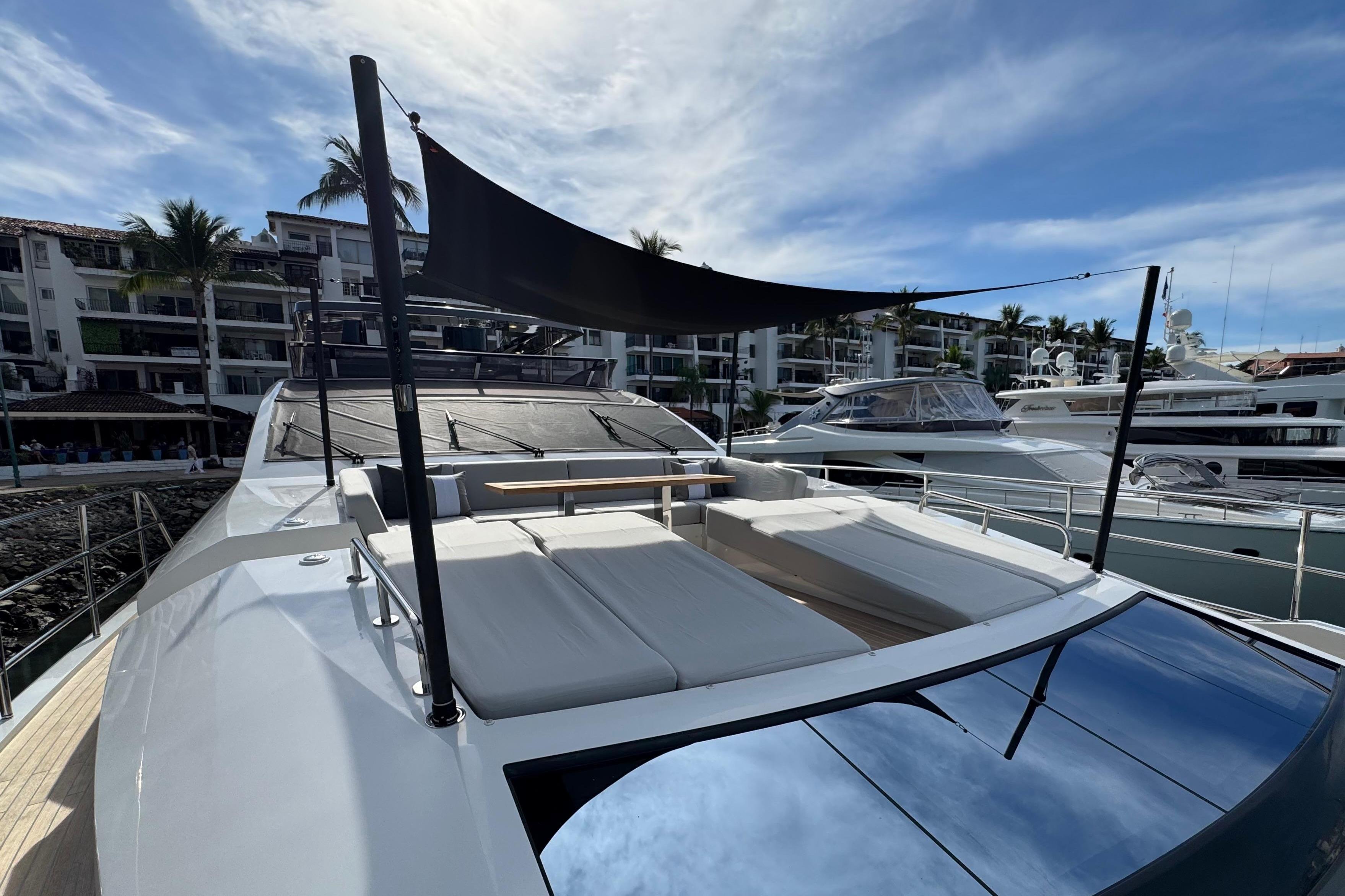 Luxurious 2023 Pearl 95 yacht with sunshade, docked at marina under blue sky.