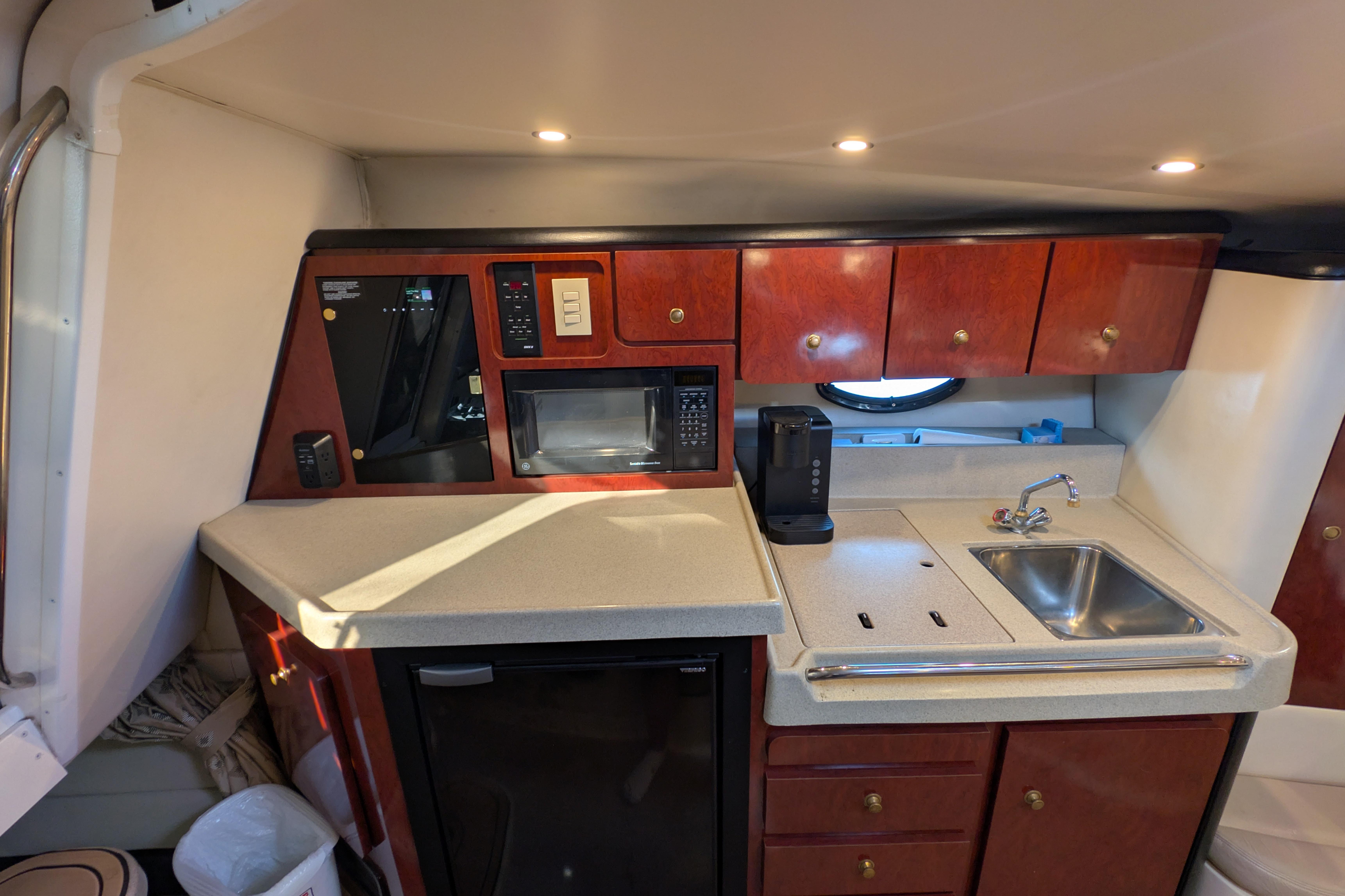 2001 Wellcraft 3300 Martinique yacht kitchen with sink, microwave, and wooden cabinets.