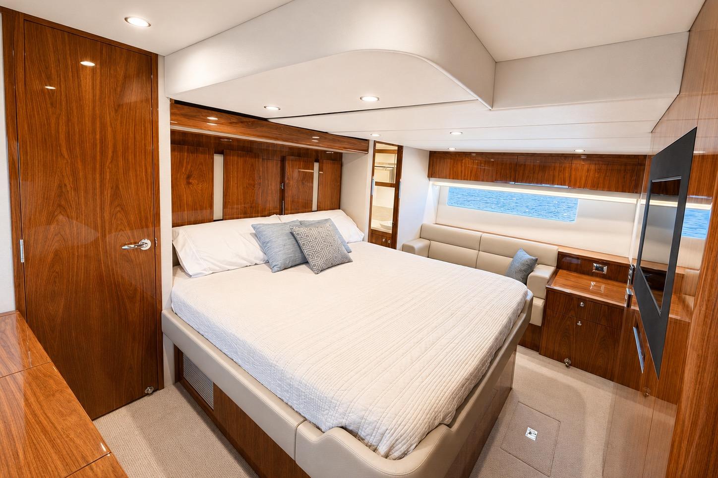Luxurious bedroom interior of 2021 Riviera 575 SUV yacht with wood finishes and ocean view.