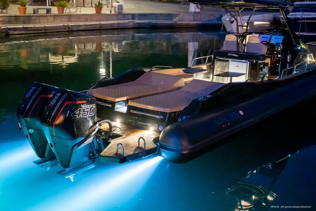 2025 SPX RIB 38 Sport boat with illuminated twin Mercury 450 engines at night.